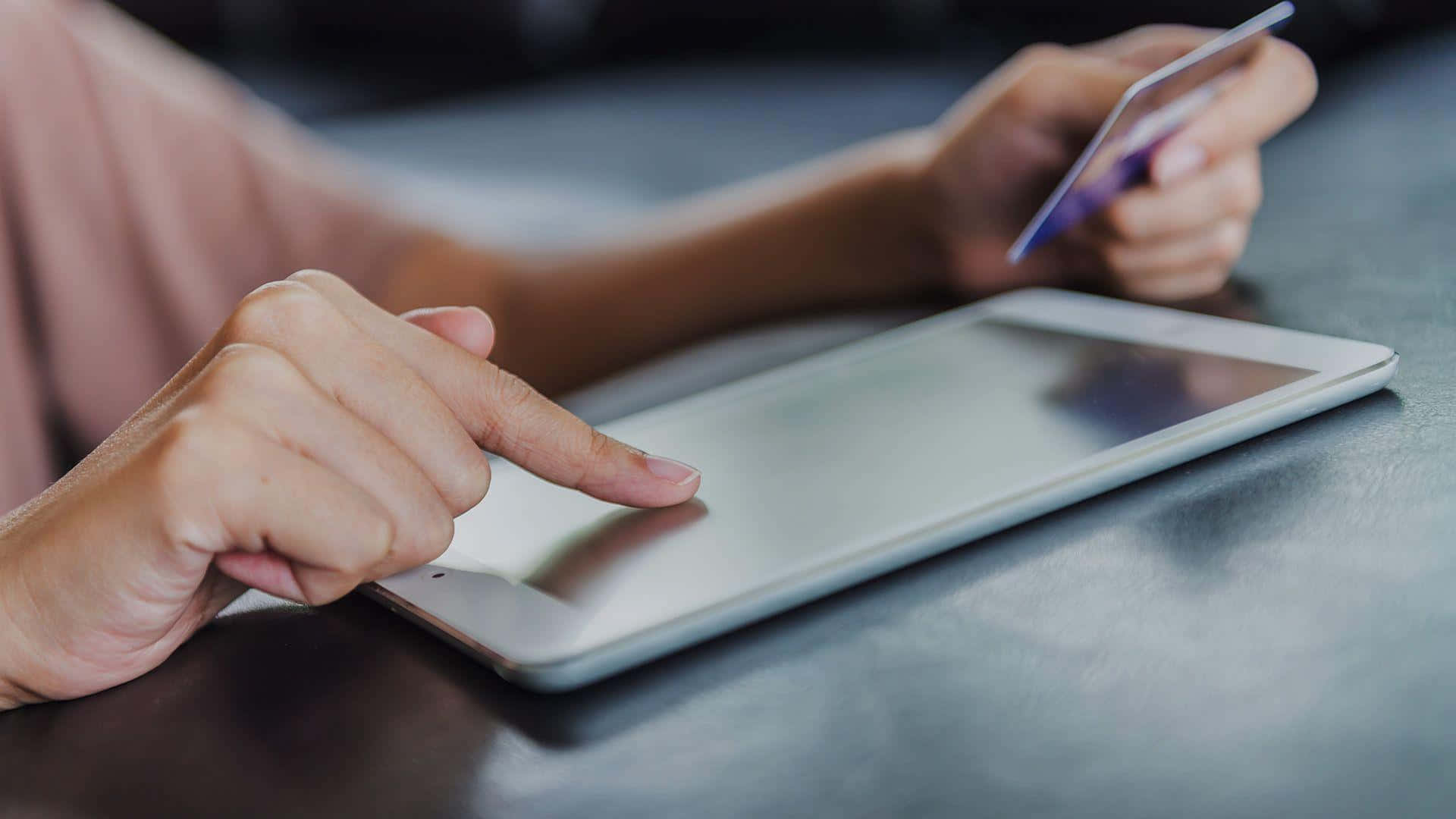 E Commerce 桌布 壁紙 — 特寫雙手在深色桌子上使用平板電腦並手持信用卡進行網上付款。