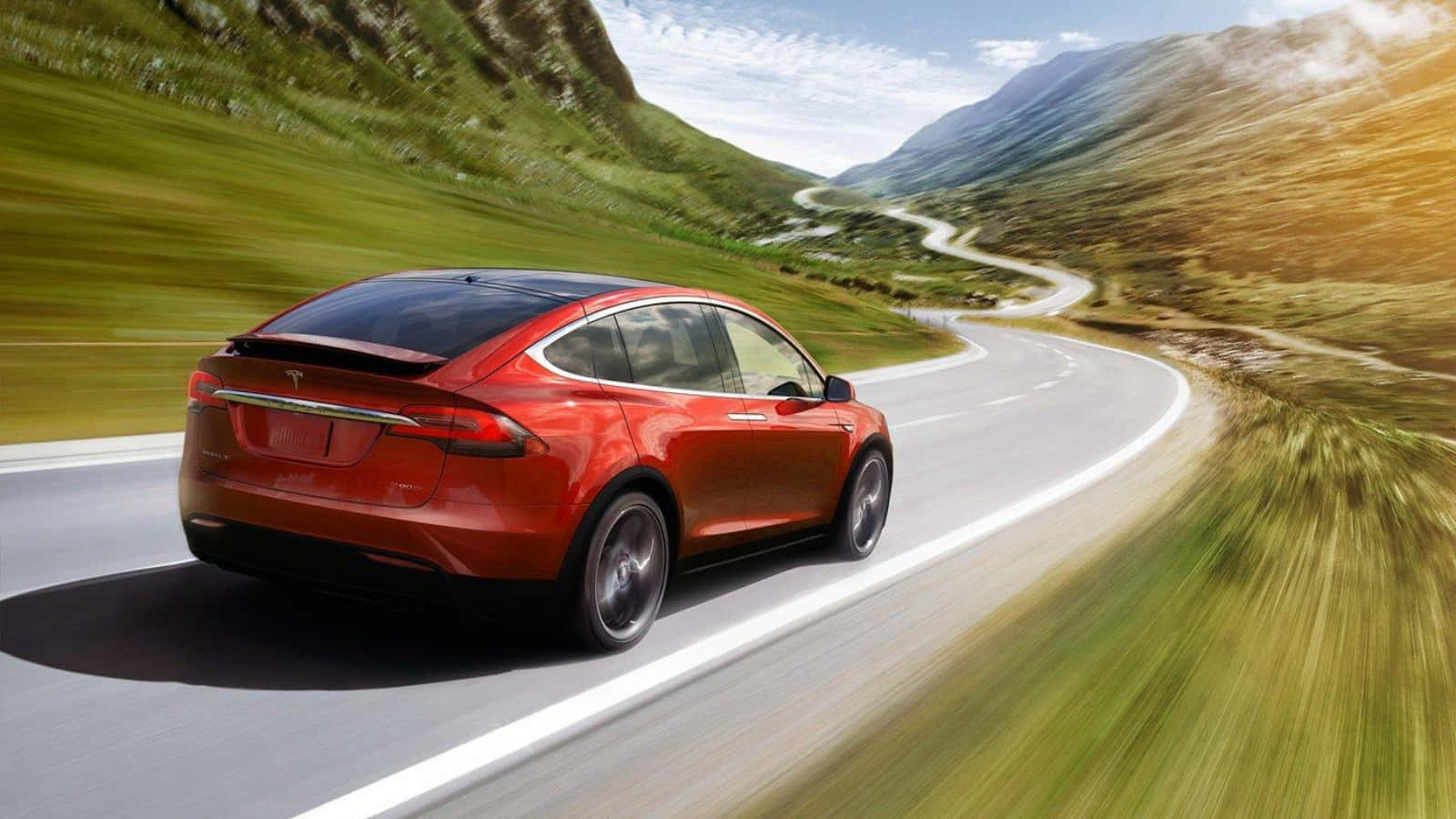 特斯拉Model 3：革命性電動車 壁紙 — 一輛鮮紅色的Tesla Model X在晴朗藍天下，沿著蜿蜒的山路穿過翠綠的山丘飛馳。