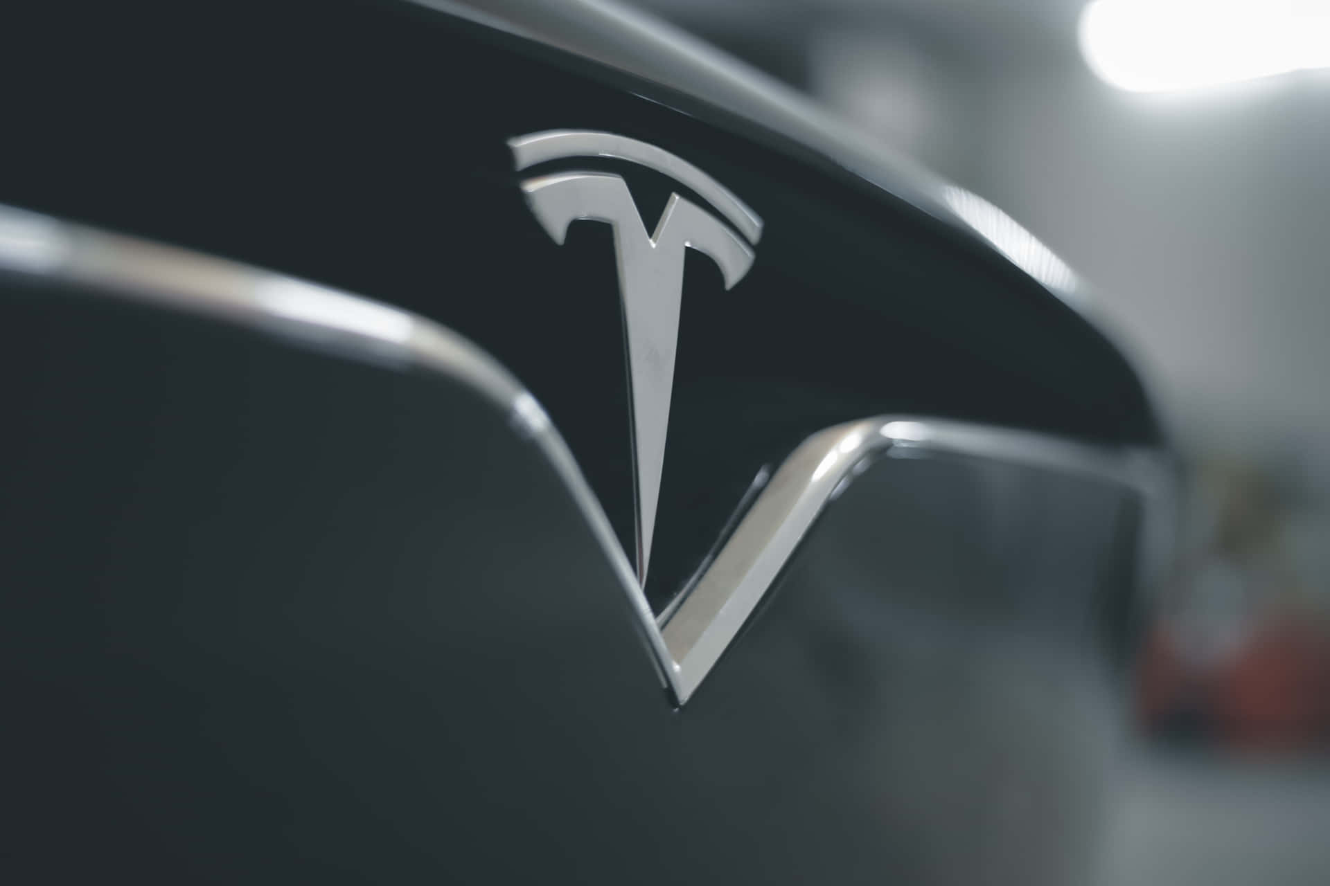 黑色車輛上閃亮的 Tesla 徽章，背景燈光模糊。
