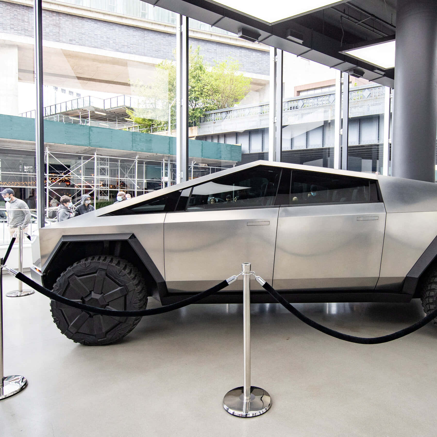 銀色Tesla Cybertruck在天鵝絨繩索和旁觀者陪同下於玻璃建築中展示。