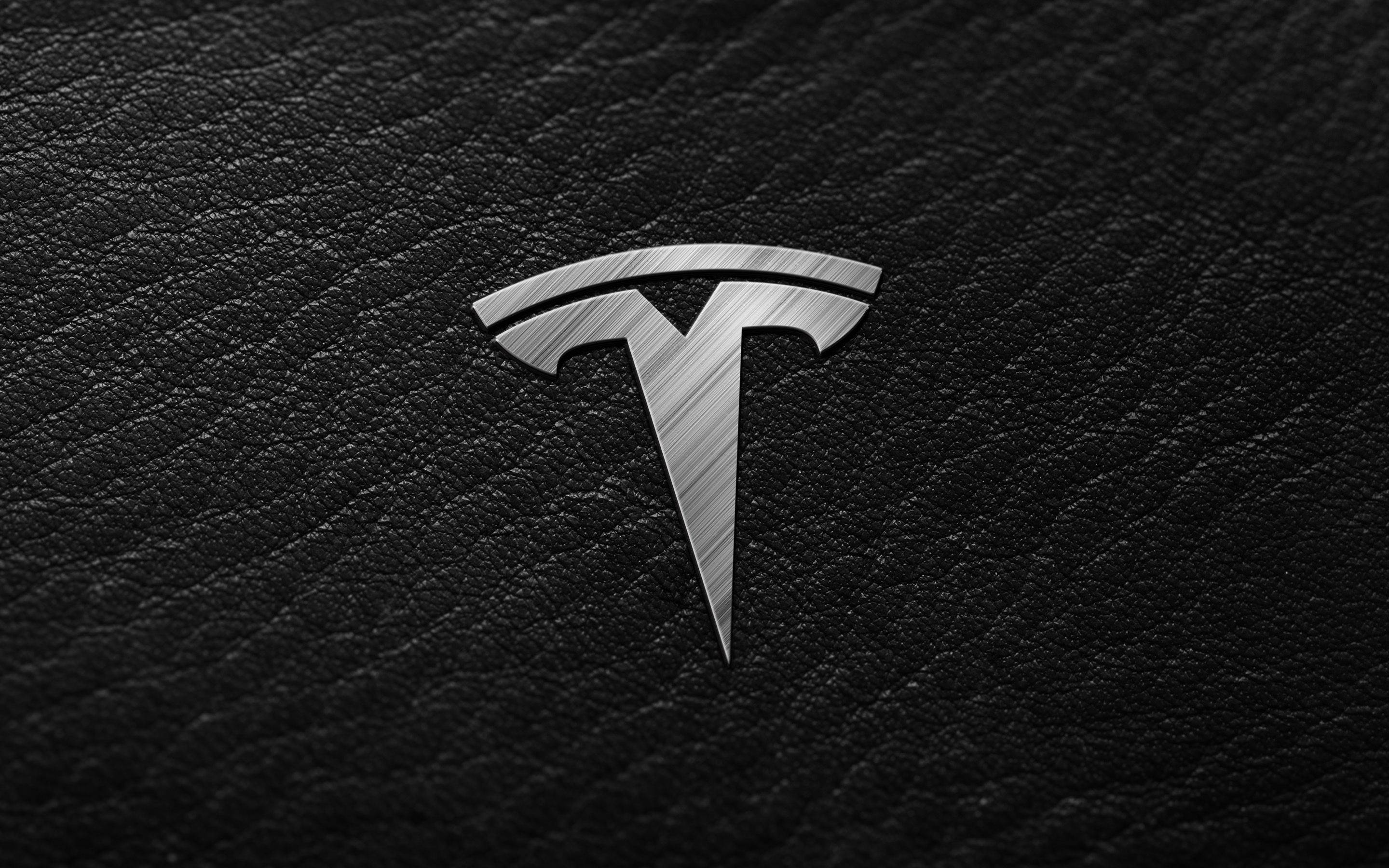 特斯拉銀色標誌 壁紙 — 一個拉絲金屬 Tesla 標誌在帶有紋理的黑色皮革背景上閃耀。