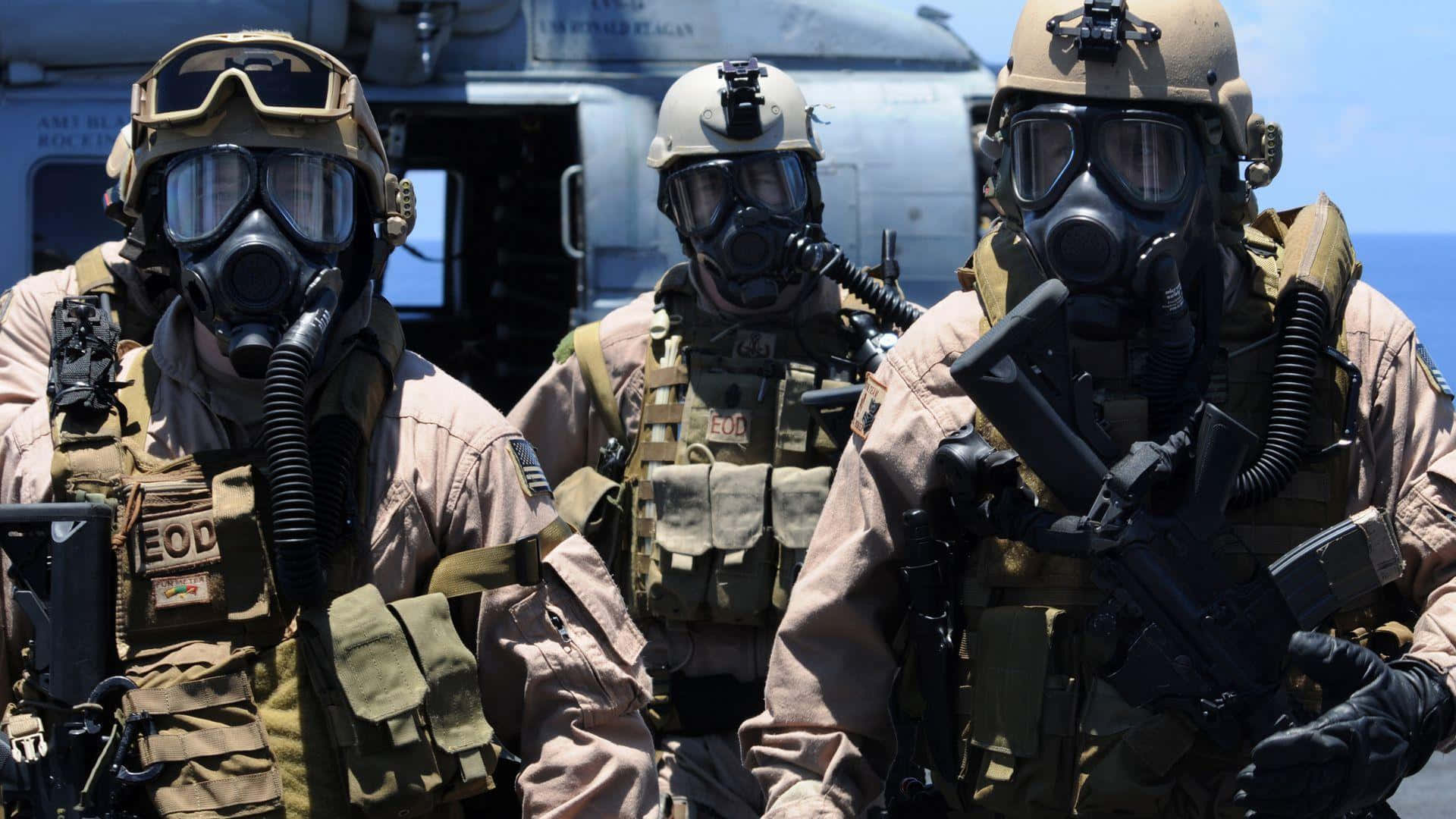 三名身穿全套裝備和防毒面具的EOD士兵站在軍用直升機附近。