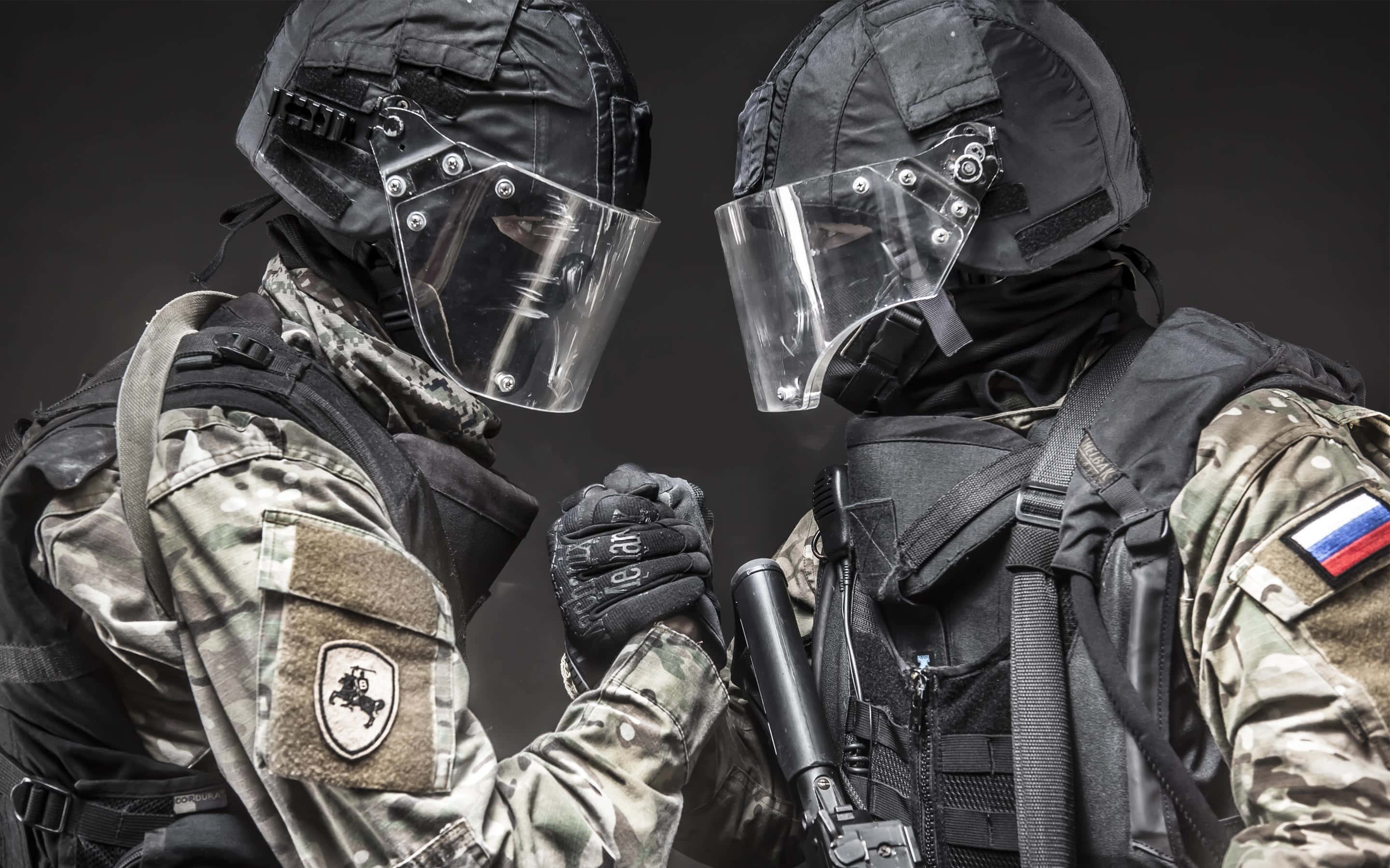 特種部隊男子面對面 壁紙 — 兩名全副武裝的戰術士兵在昏暗的攝影棚環境中鎖拳，可見國家臂章。