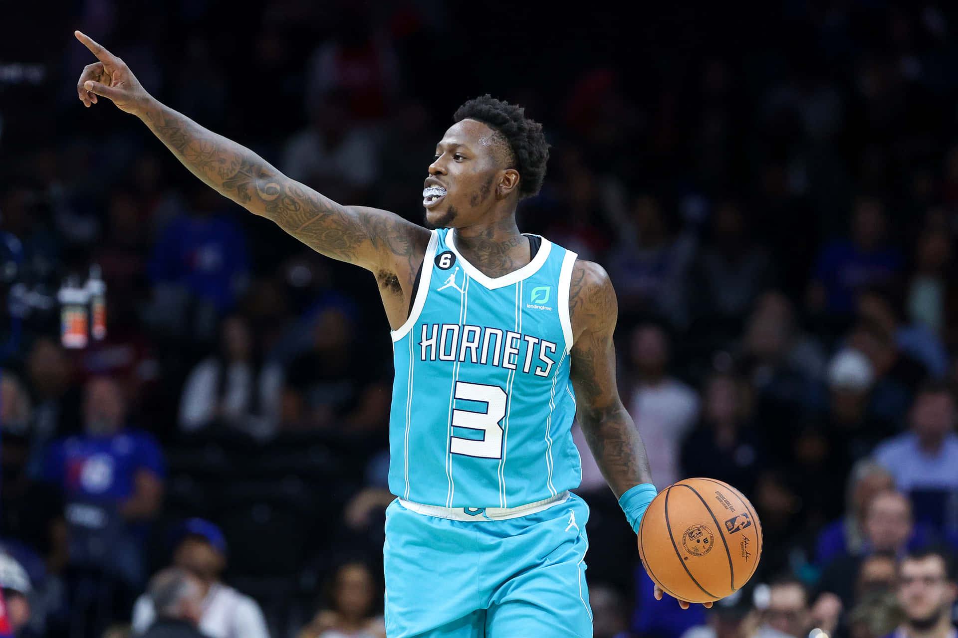 特里·羅齊爾 NBA 球員 壁紙 — 一位身穿青綠色球衣的夏洛特黃蜂隊籃球運動員在場館燈光下比賽時，手持籃球向上指。