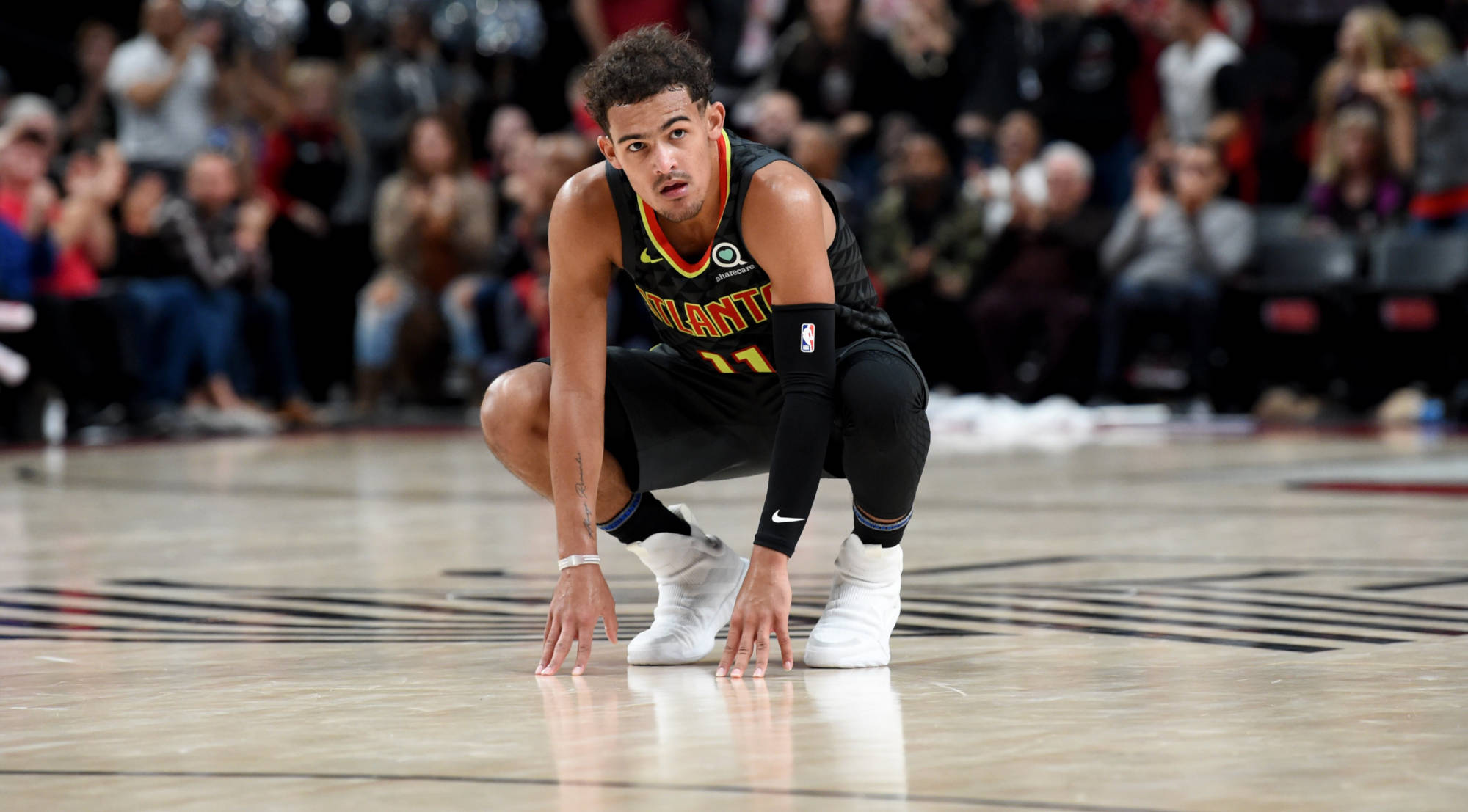 特雷·楊NBA東部聯賽 壁紙 — 一名身穿亞特蘭大球衣的籃球運動員在比賽中跪在球場上，雙手放在地上，背後是模糊的人群。