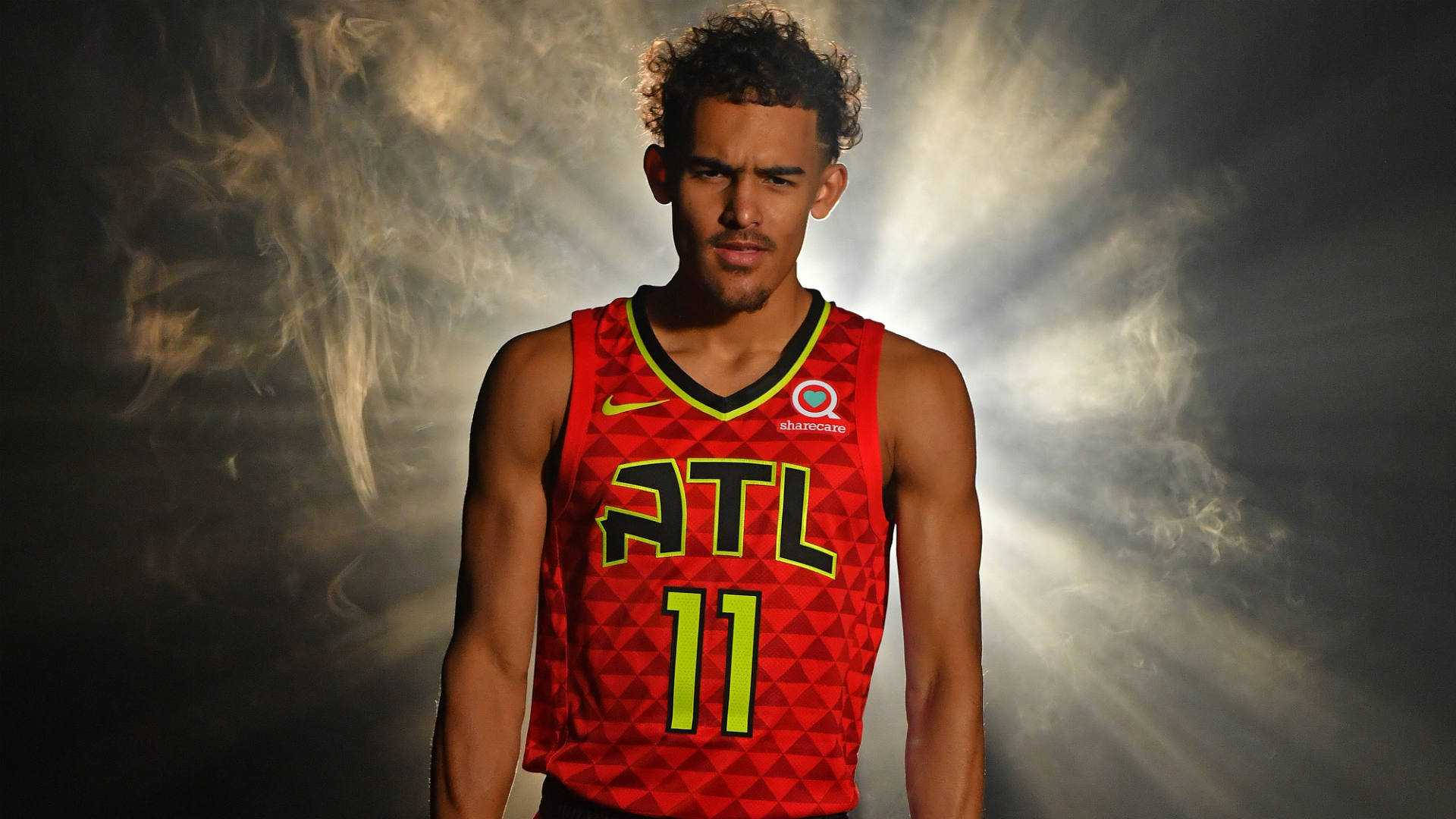 特雷·楊NBA老鷹隊 壁紙 — 一名身穿紅色亞特蘭大老鷹隊球衣的籃球運動員，自信地站在煙霧瀰漫、光線四射的戲劇性背景前。