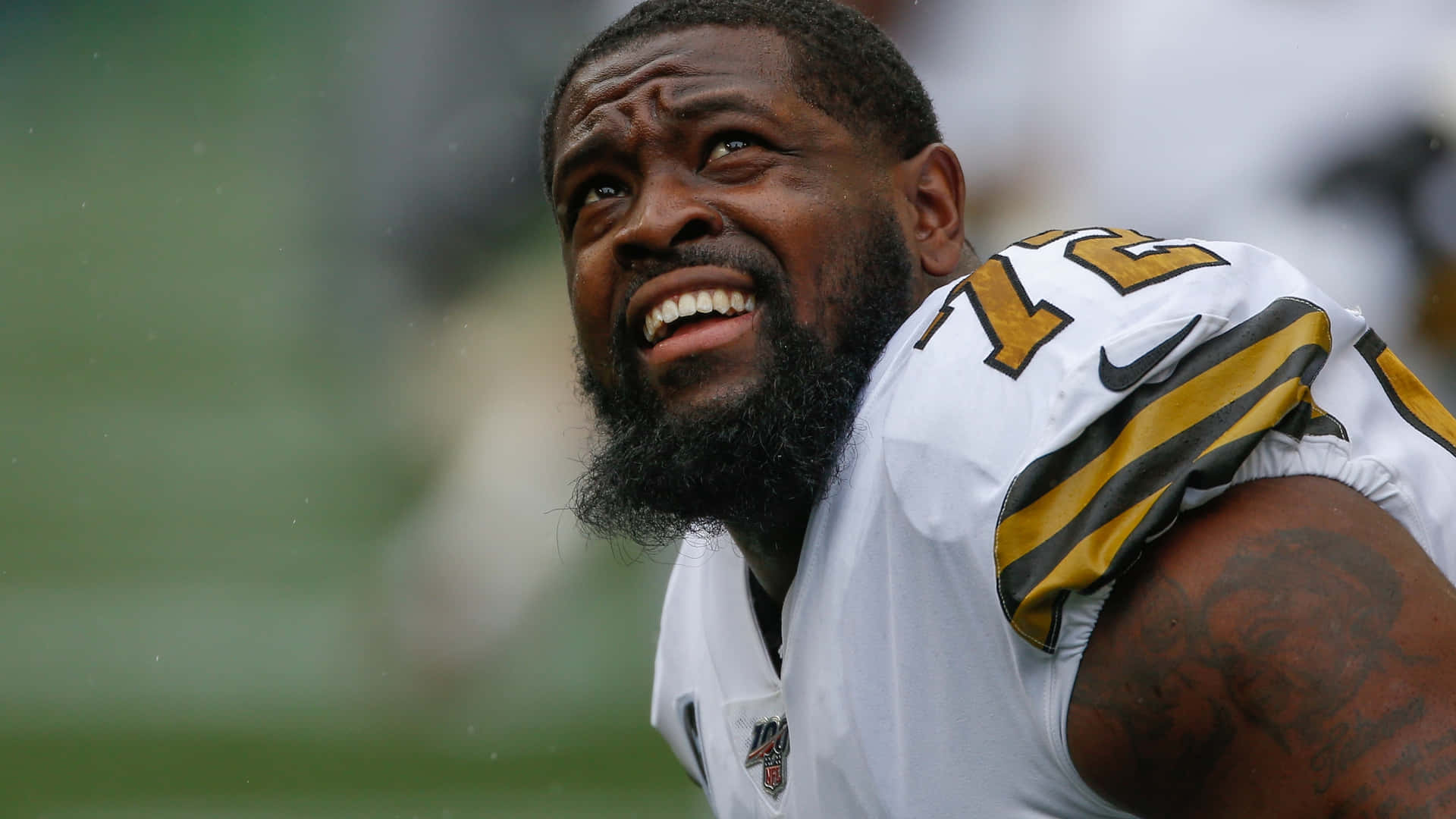 特龍·阿姆斯特德 新奧爾良聖徒隊 NFL 球員 壁紙 — 一位鬍鬚足球員身穿白色金色球衣，在雨中的球場上大笑的特寫。