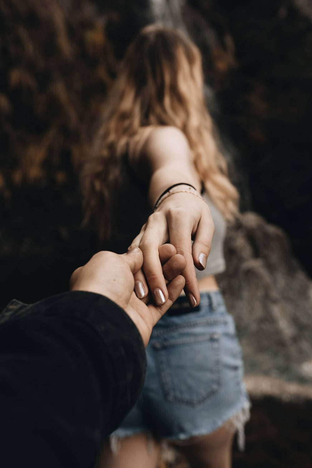 牽手帶領他離開的女孩 壁紙 — 兩隻手緊握的特寫，背後是瀑布傾瀉而下，一位身穿牛仔短褲的女性。
