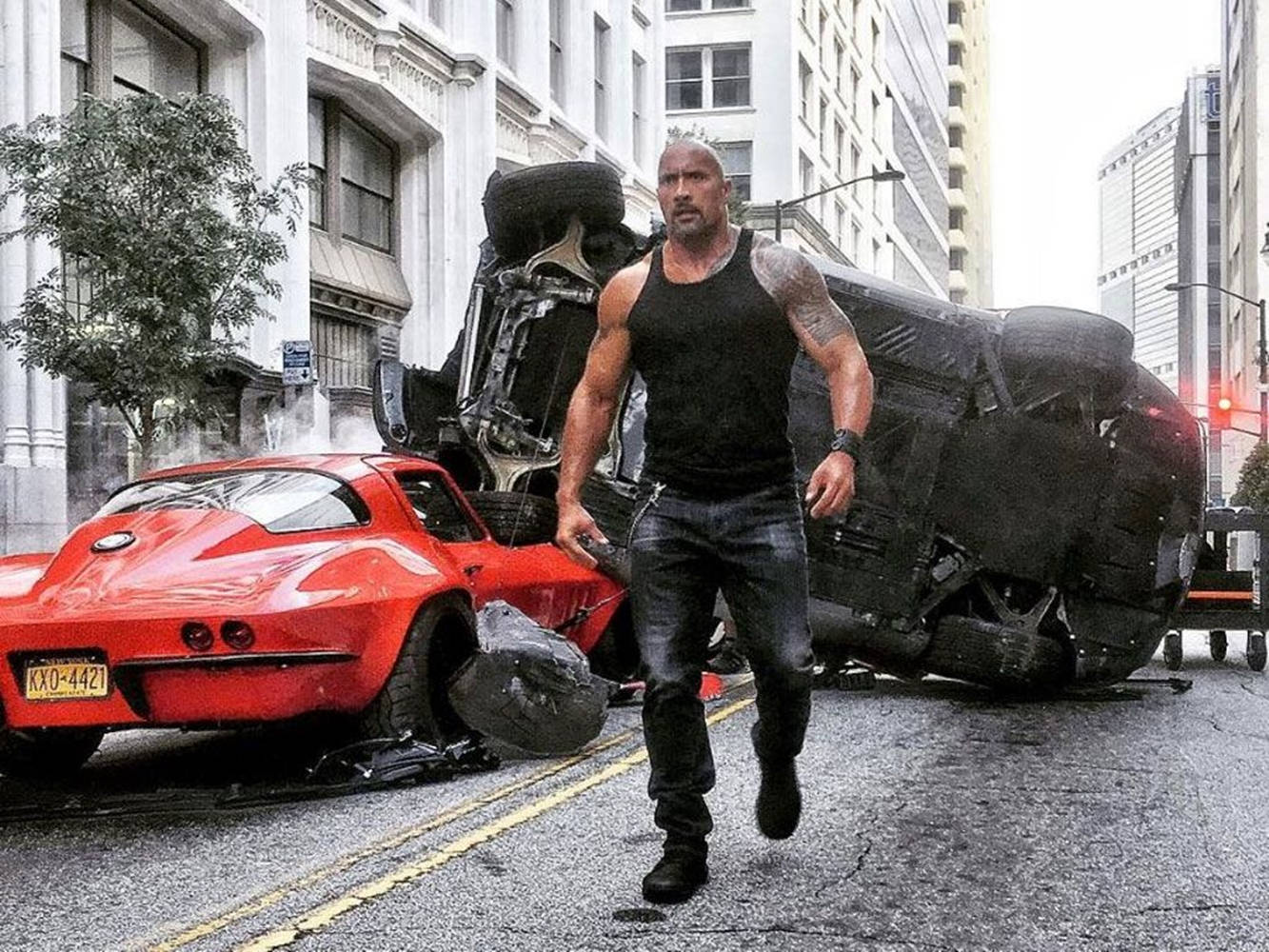 The Rock 桌布 壁紙 — 狄維莊遜喺城市混亂中，行過一輛紅色跑車同一輛翻轉嘅黑色車，喺城市街道上大步前行。