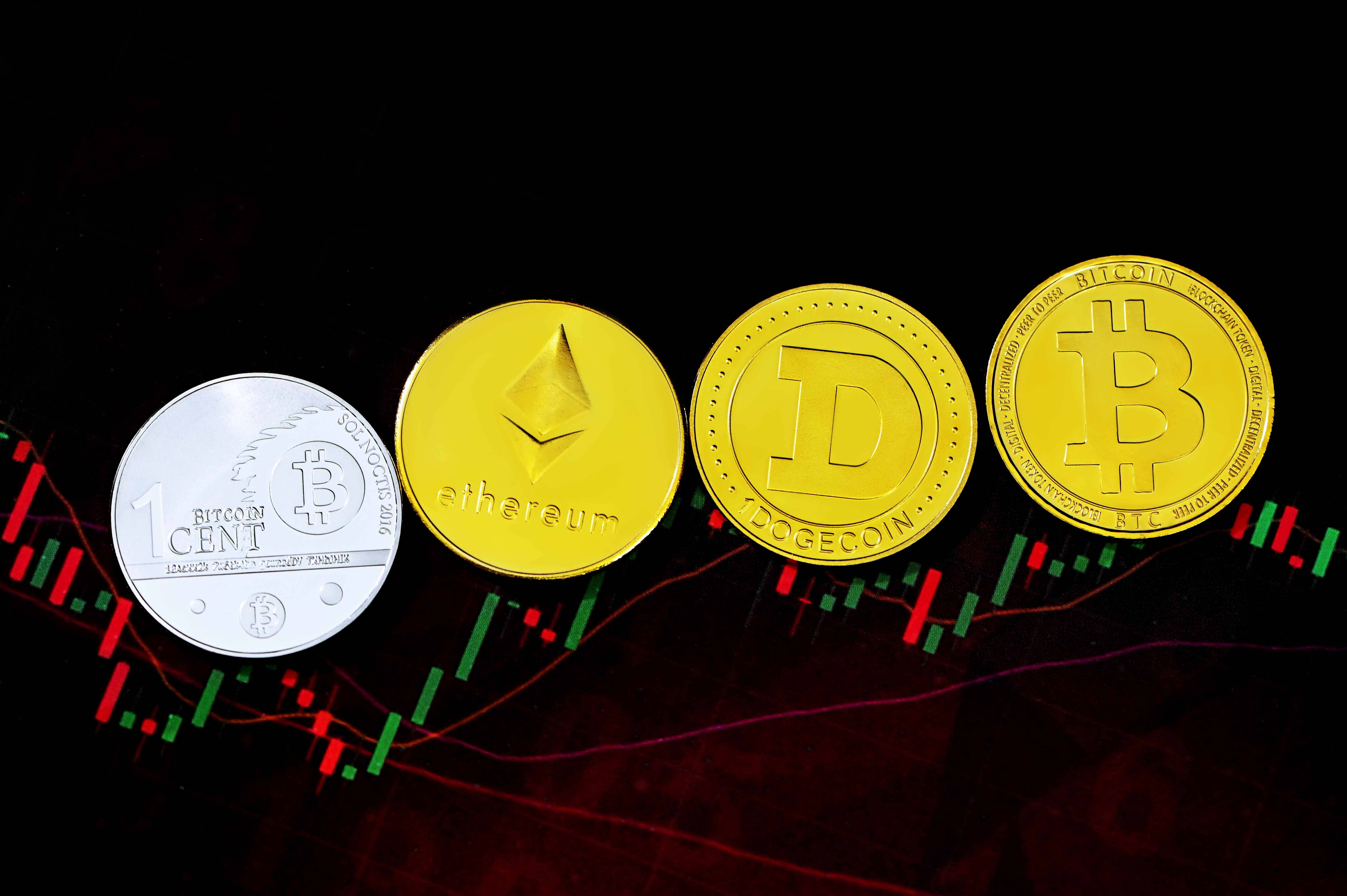 狗狗幣加密貨幣數位圖表 壁紙 — 四個實體加密貨幣硬幣 Bitcoin Ethereum Dogecoin 和一個銀色 Bitcoin 仙硬幣放在一個發光的股票圖表上，帶有紅色和綠色條形。