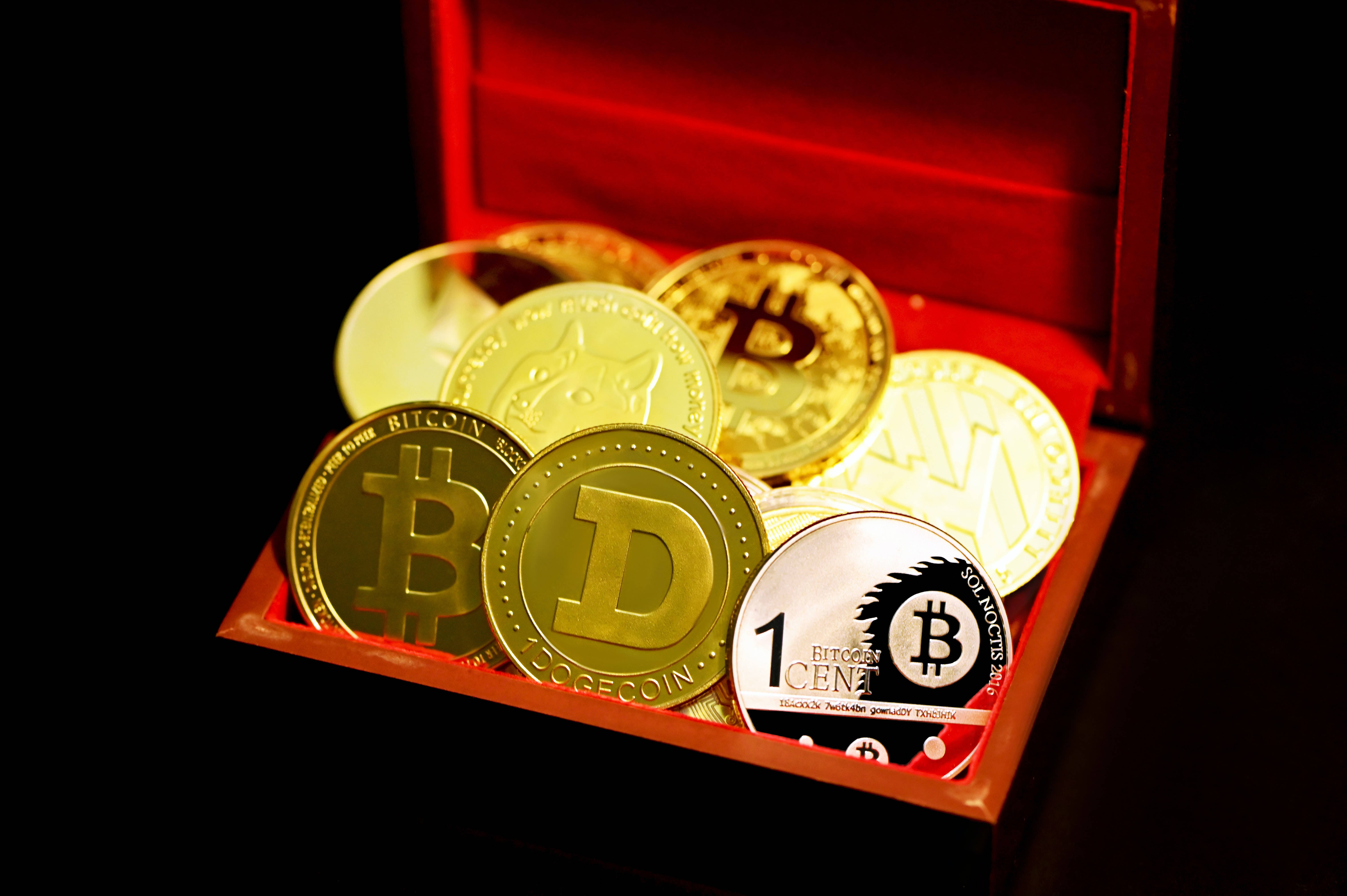 狗狗幣藏於寶盒 壁紙 — 金色加密貨幣硬幣，包括比特幣和狗狗幣，在黑色背景上的一個打開的紅色木製寶箱內溫暖地發光。