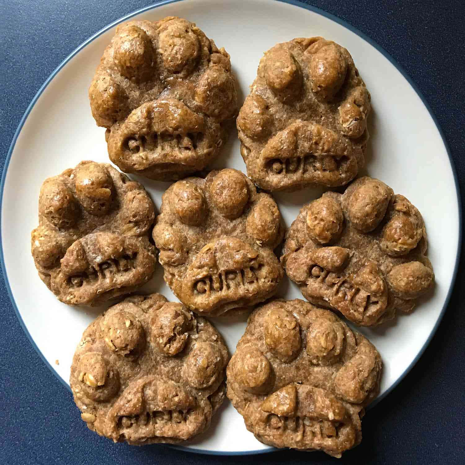 七塊印有 'GURLY' 的爪形狗零食放在白色碟子上。