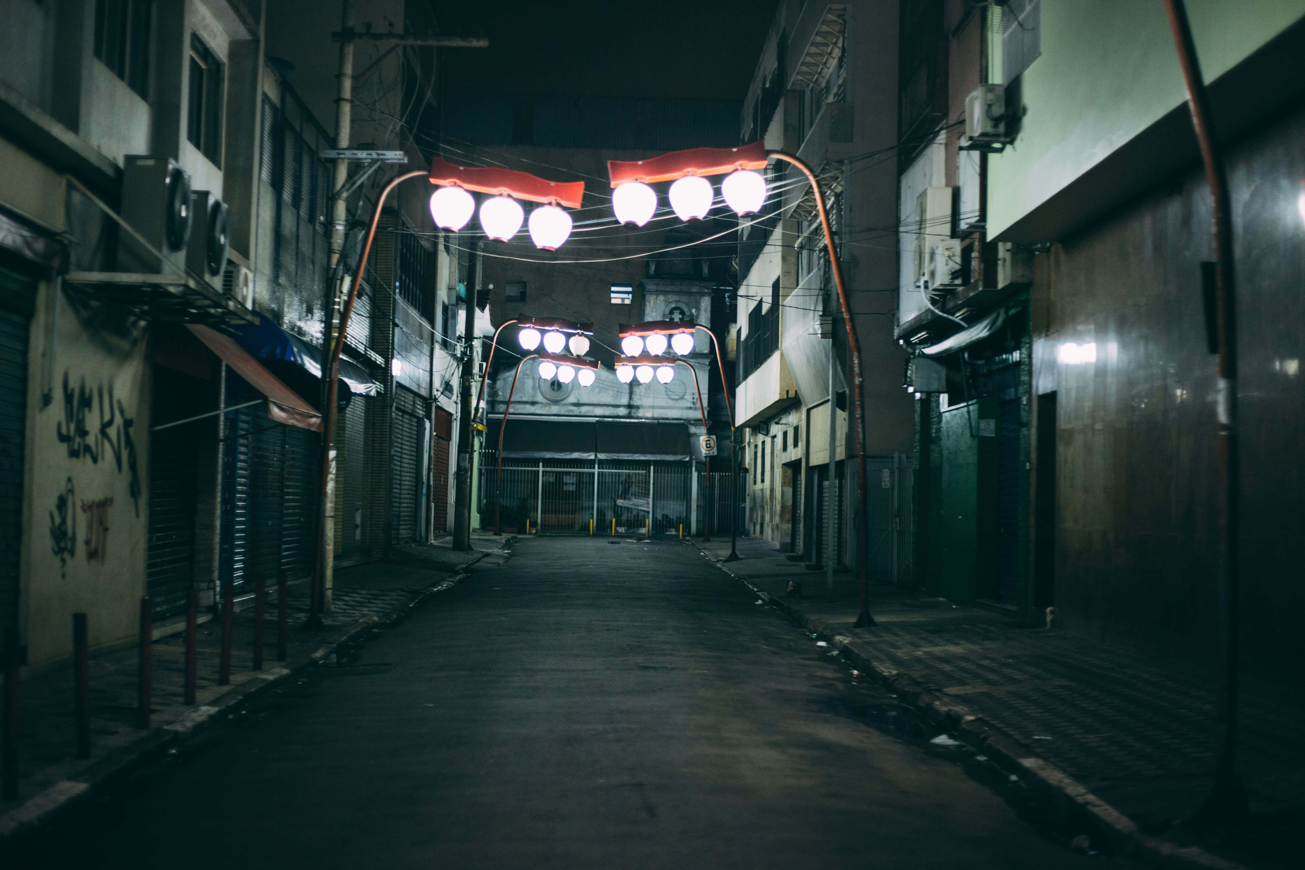 Alleyway 桌布 壁紙 — 狹窄的城市小巷在夜晚被發光的頭頂燈照亮，在潮濕的路面上投下長長的影子。
