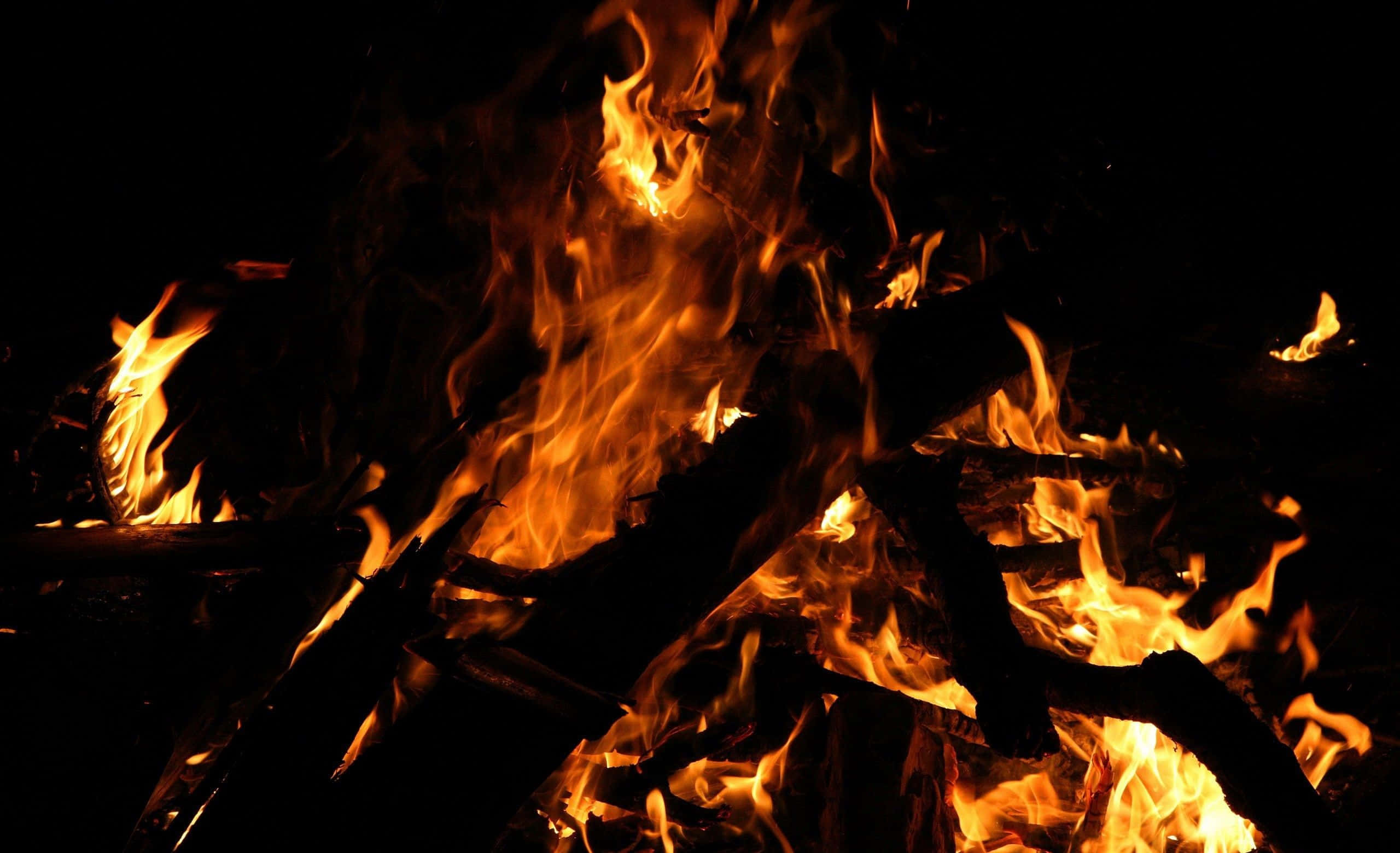 Campfire 桌布 壁紙 — 猛烈的火焰在漆黑的夜空下，於焦黑的木頭上跳躍並發出噼啪聲。