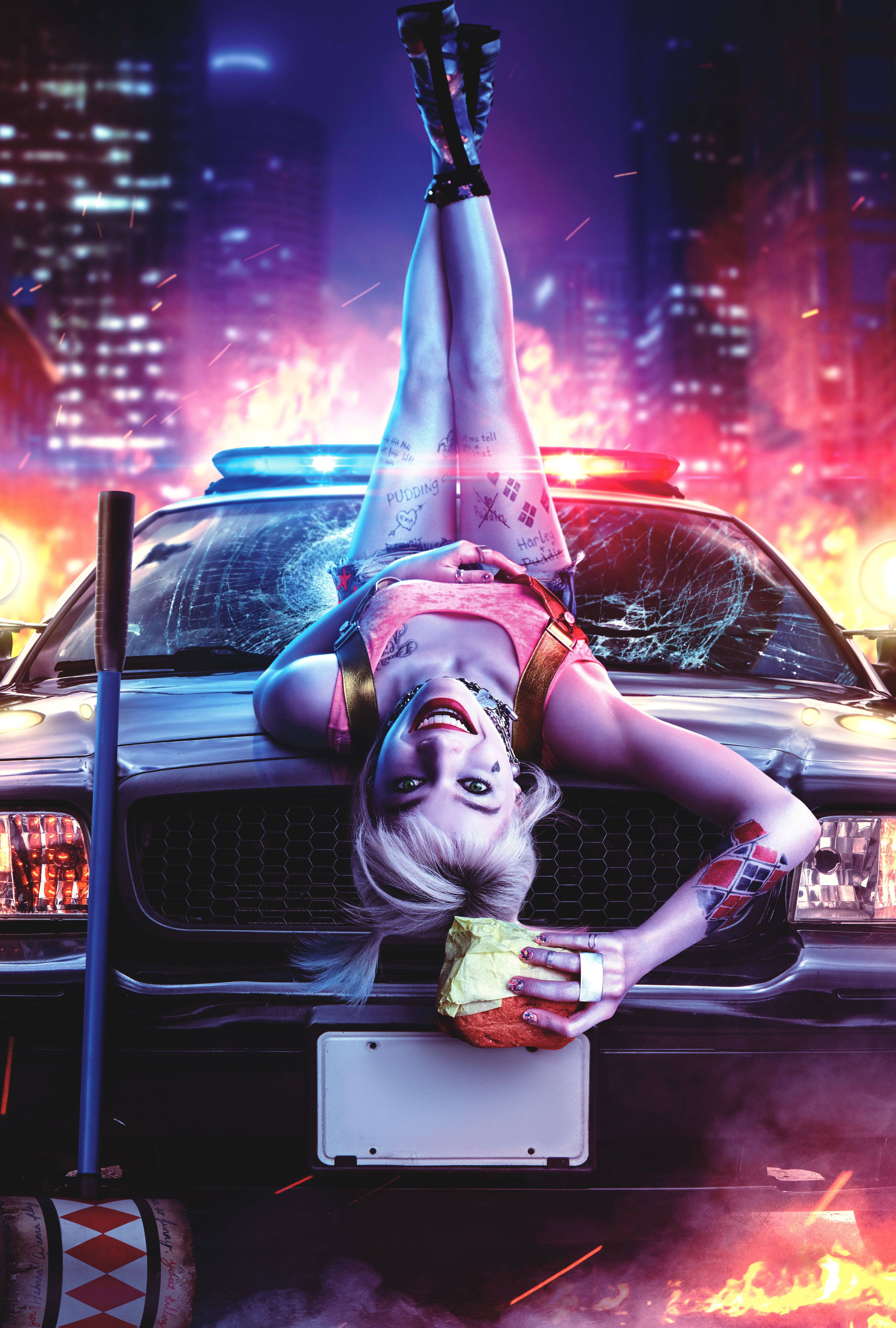 《猛禽小隊》哈莉躺警車車頭 壁紙 — 一名金髮女子在夜晚的火焰霓虹城市景觀中倒掛在警車上。