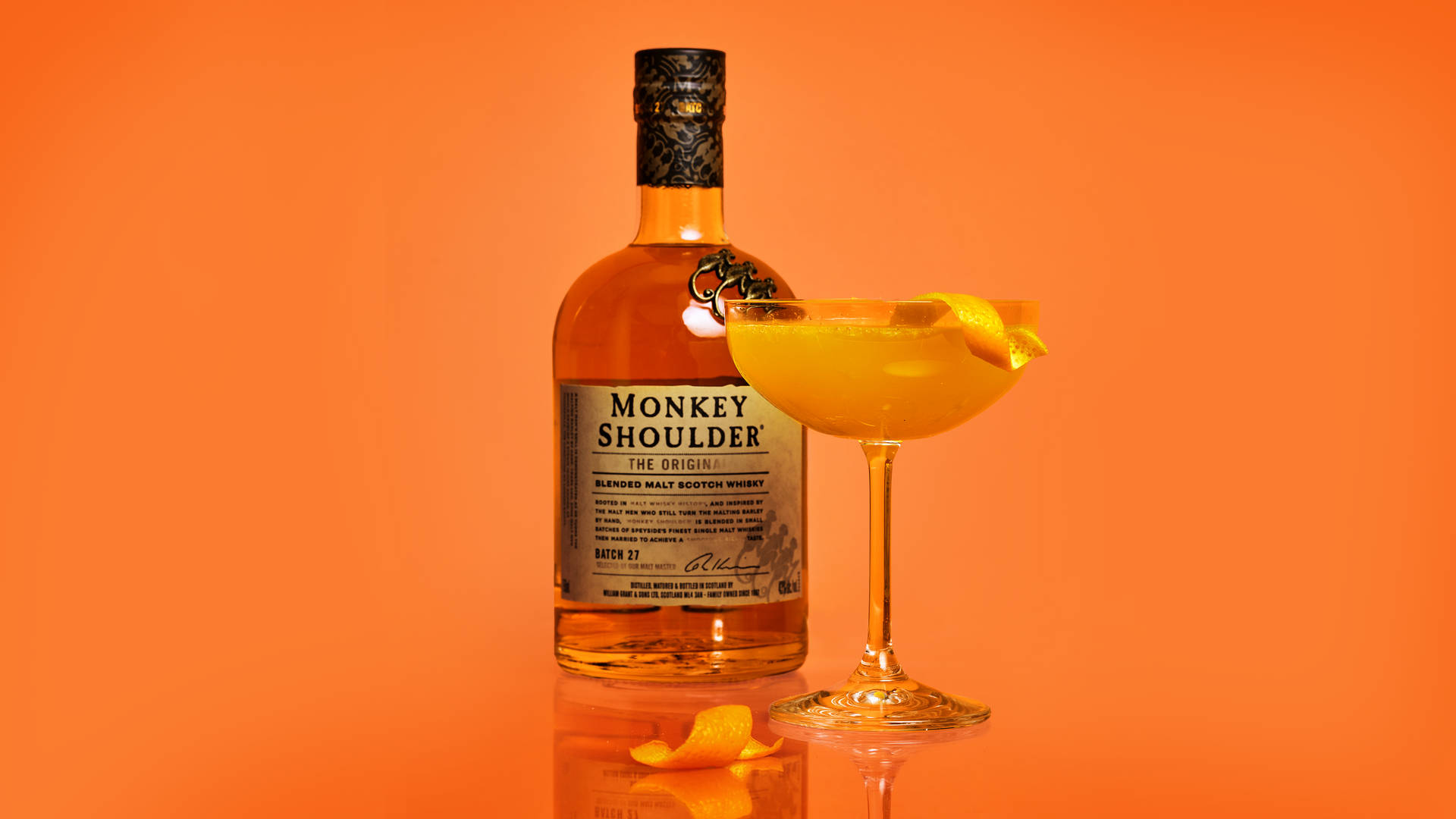 Monkey Shoulder威士忌瓶和橙色雞尾酒在反光表面上，橙色背景。