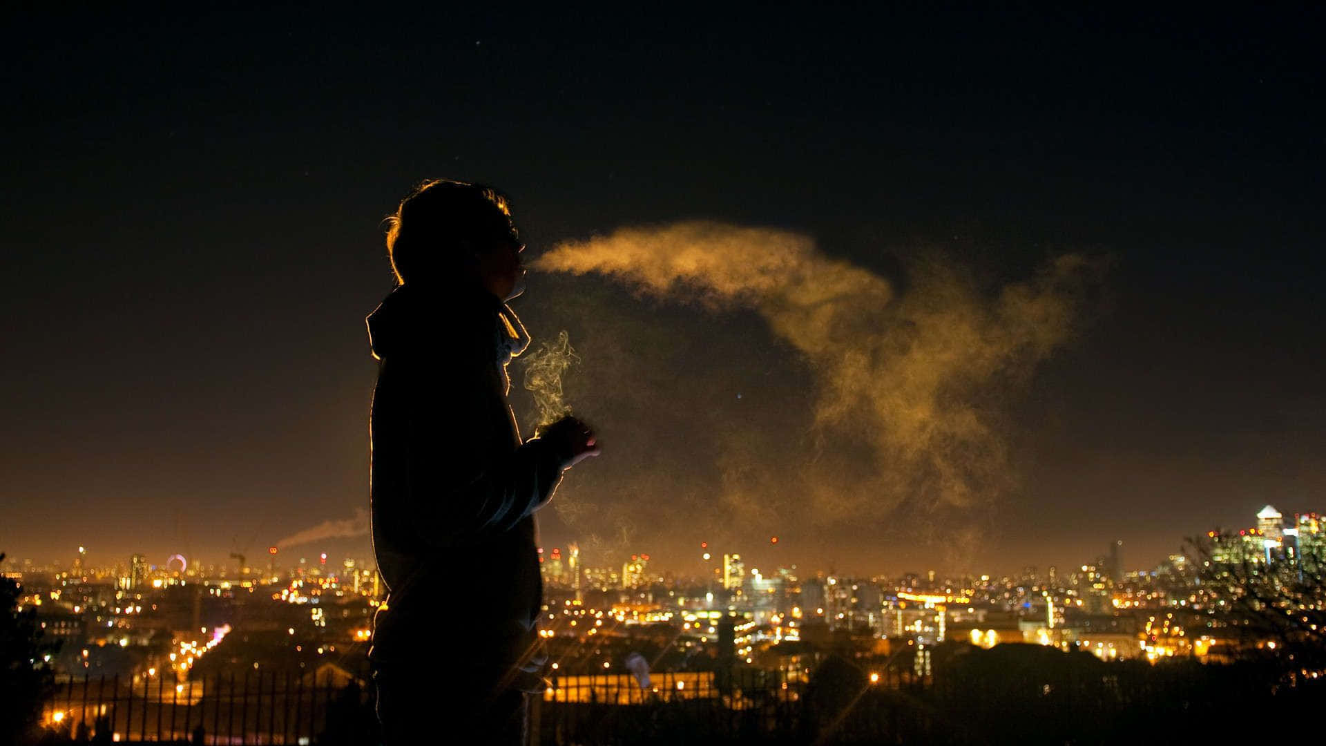 一個人在夜間對著發光的城市呼出蒸氣。
