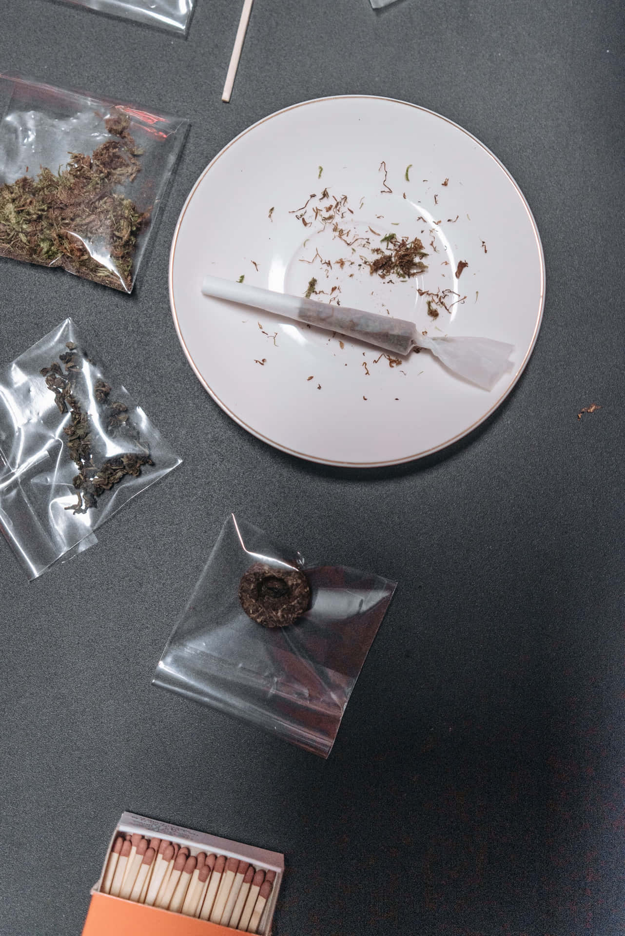 用過的大麻煙捲在碟上，有香草袋和火柴在深色表面。
