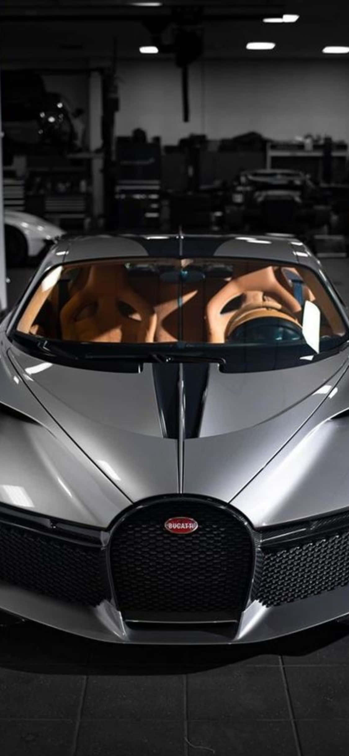 獨特奢華：以個人化 iPhone XS 與布加迪探索世界 壁紙 — 一架時尚的銀色 Bugatti 超級跑車配備棕色皮革座椅，停放在天花燈下光線昏暗的車庫中。