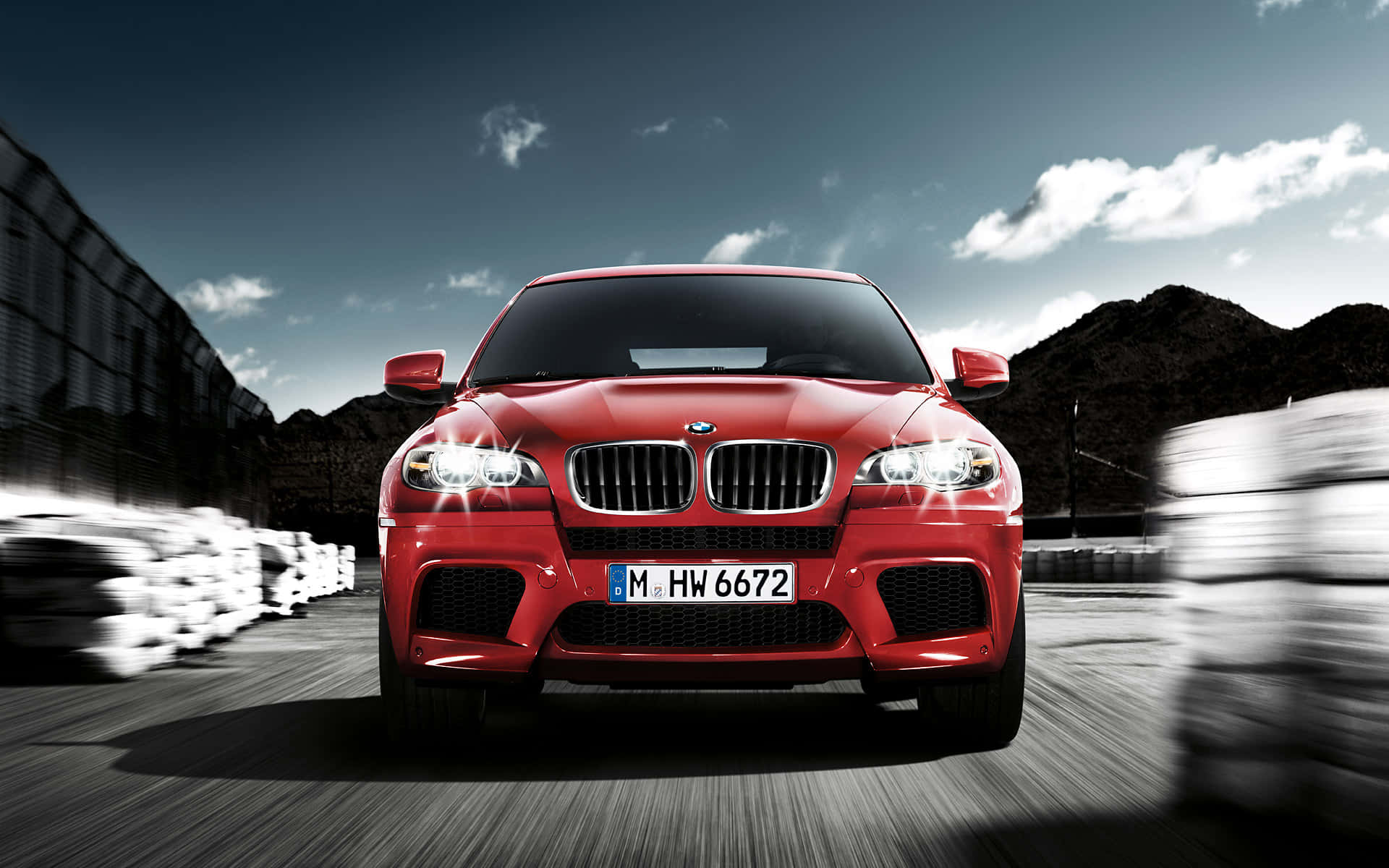 獨特而強勁的 BMW X6 M 壁紙 — 一輛充滿活力的紅色BMW M1跑車在賽道上疾馳，帶有動態模糊和戲劇性的天空。