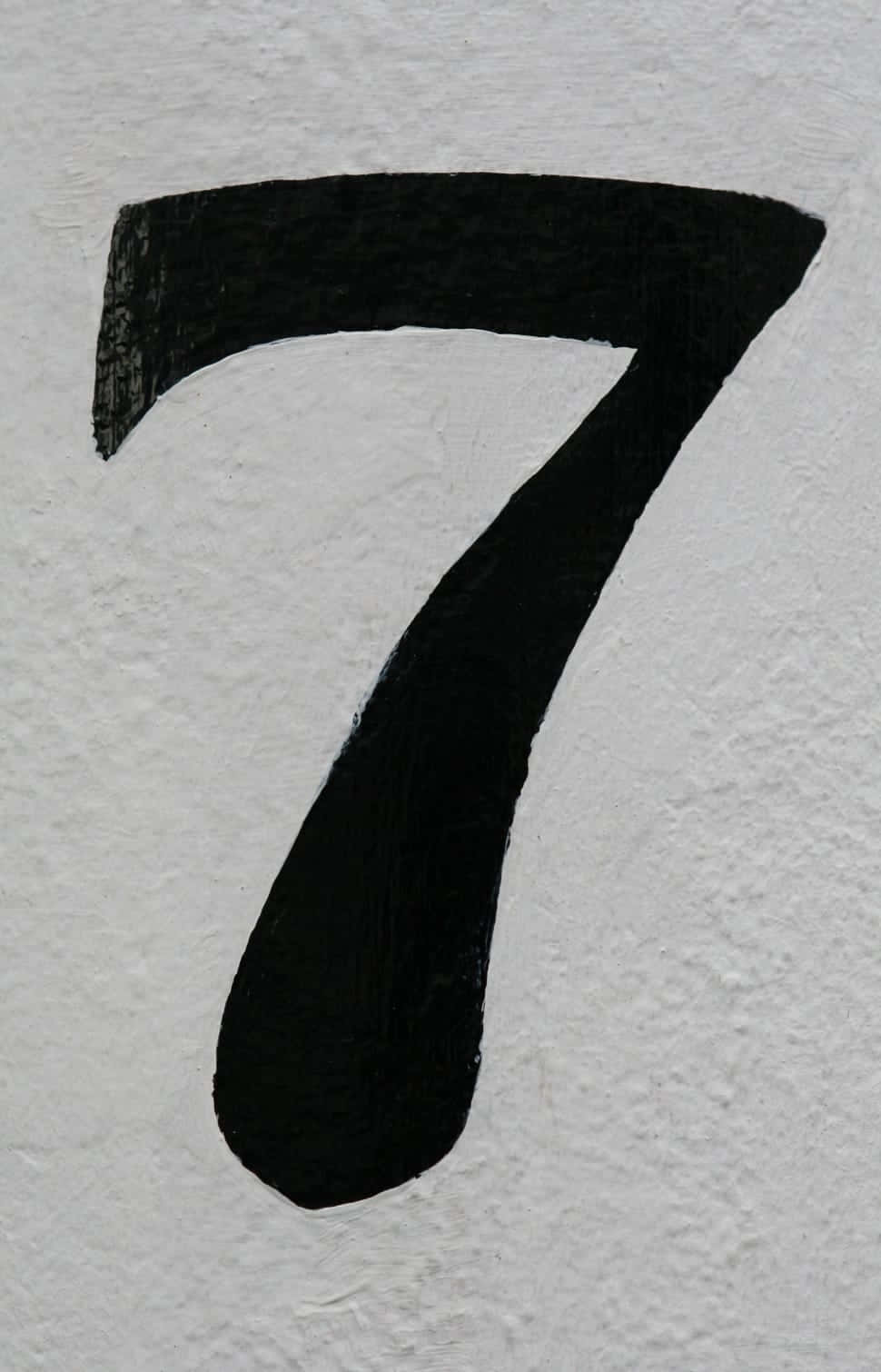 獨特設計的數字七 壁紙 — 一個大膽的黑色數字七，塗在粗糙的白色紋理牆上，可見筆觸。