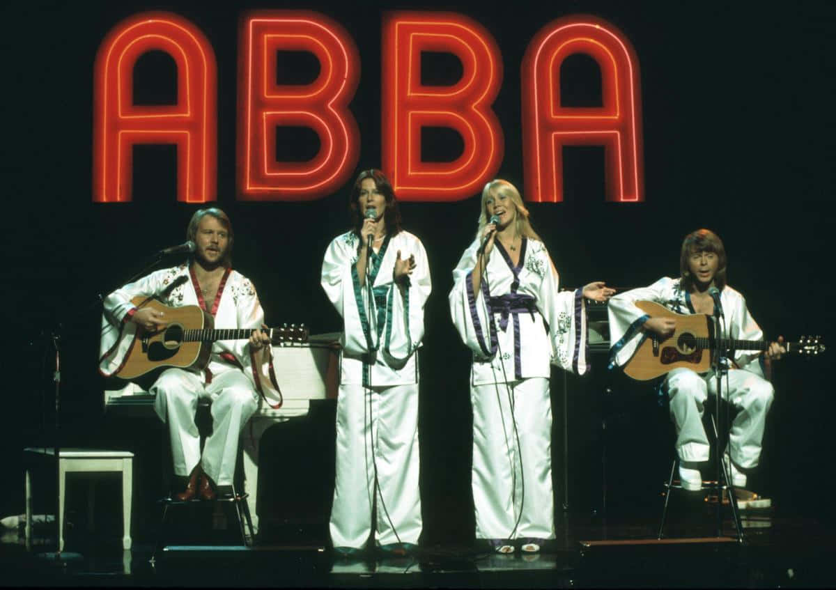 ABBA樂隊身穿白色服裝在紅色霓虹燈牌下現場表演。