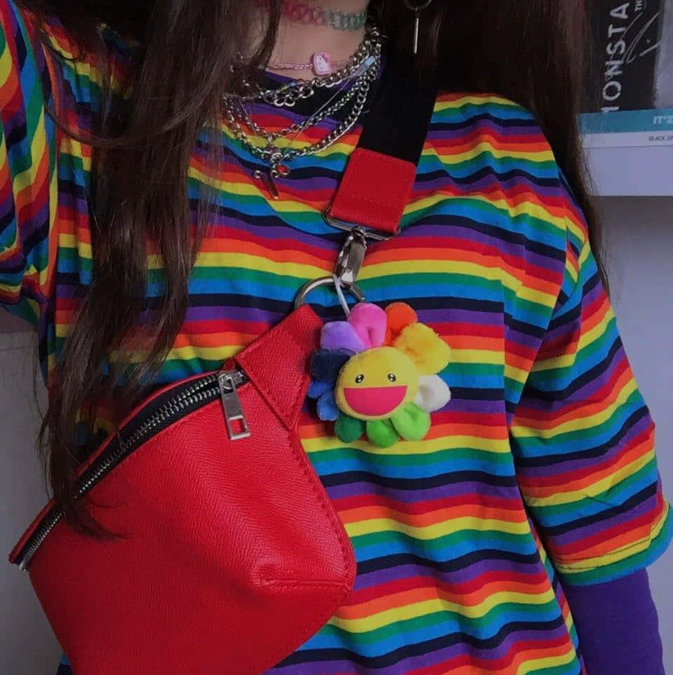 獨立風格彩虹服飾宣言 壁紙 — 一個人穿著鮮豔的彩虹條紋襯衫，並攜帶一個飾有開心微笑花朵公仔的紅色斜孭袋。