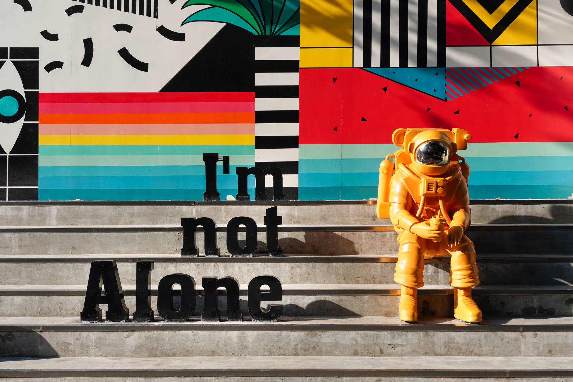 樓梯上嘅橙色太空人雕像，配色彩繽紛壁畫同「I'm not Alone」文字。