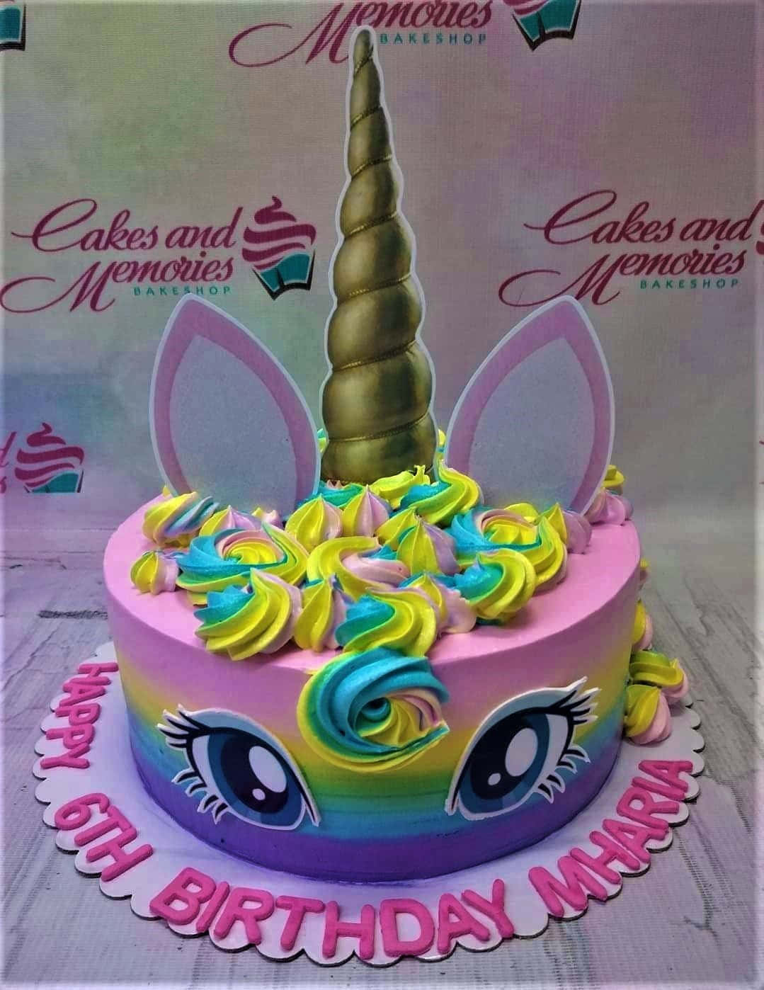 獨角獸主題生日蛋糕 壁紙 — 一個充滿活力的獨角獸主題生日蛋糕，帶有彩虹糖霜眼睛和金色角，放在粉紅色扇貝形板上。