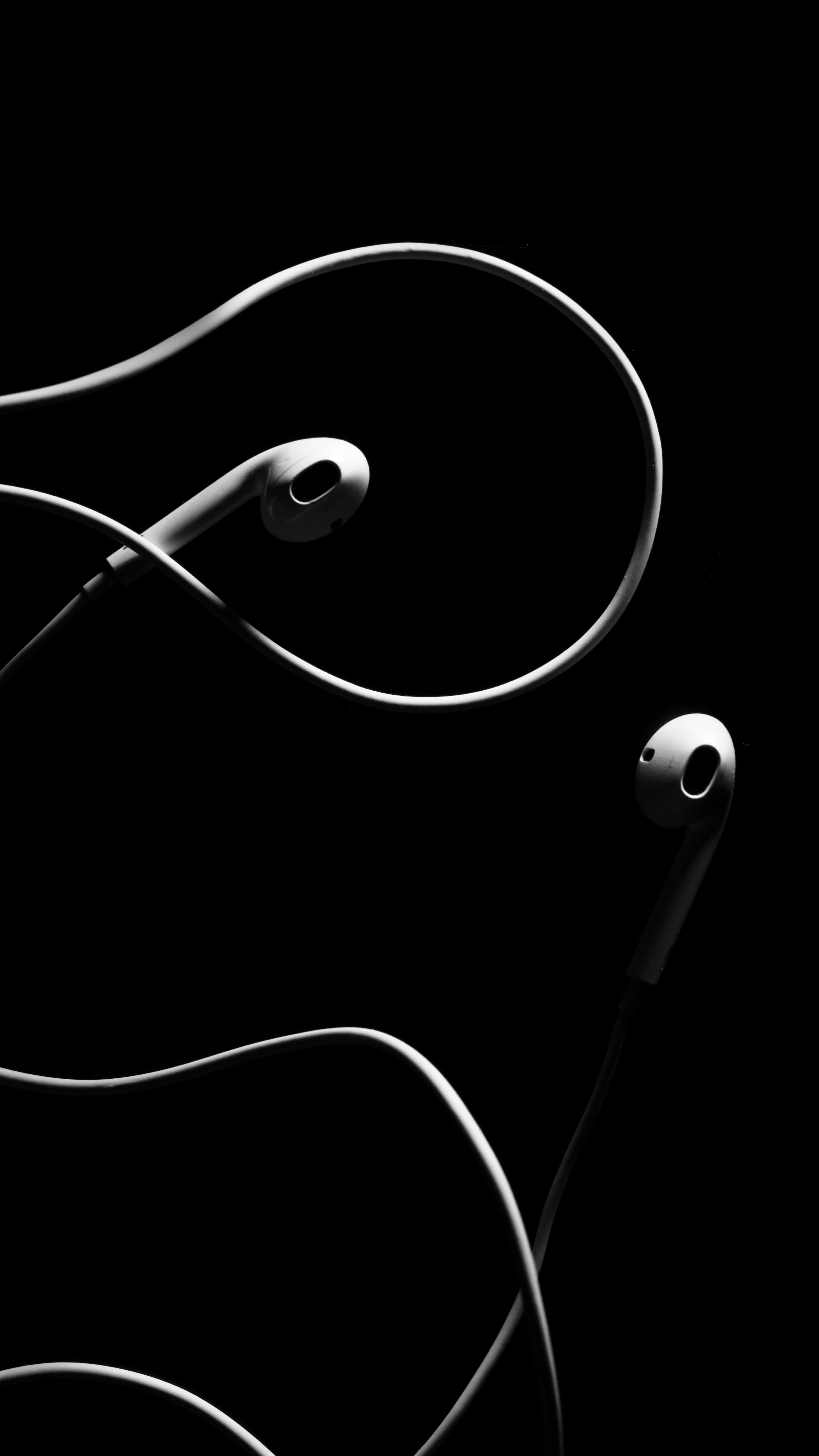 獲取最新黑色版iPhone，保持時尚科技外觀 壁紙 — 時尚的白色耳塞搭配螺旋線纜，在純黑背景上優雅彎曲，呈現高對比度的單色效果。