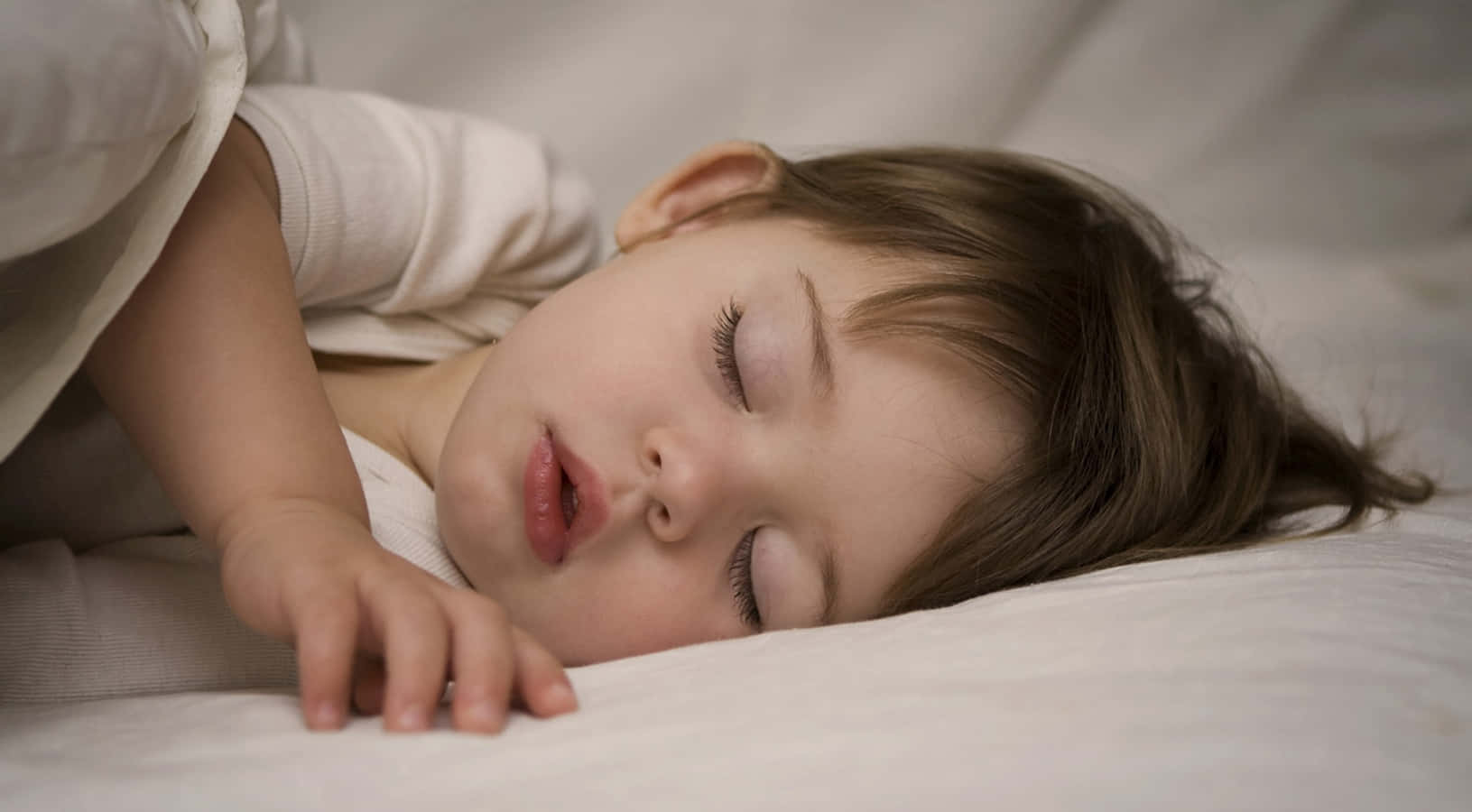 獲得身體所需的寧靜睡眠 壁紙 — 一個平靜嘅幼兒喺柔軟嘅白色枕頭上閉上眼睛，手輕輕放喺面頰旁邊，睡得香甜。