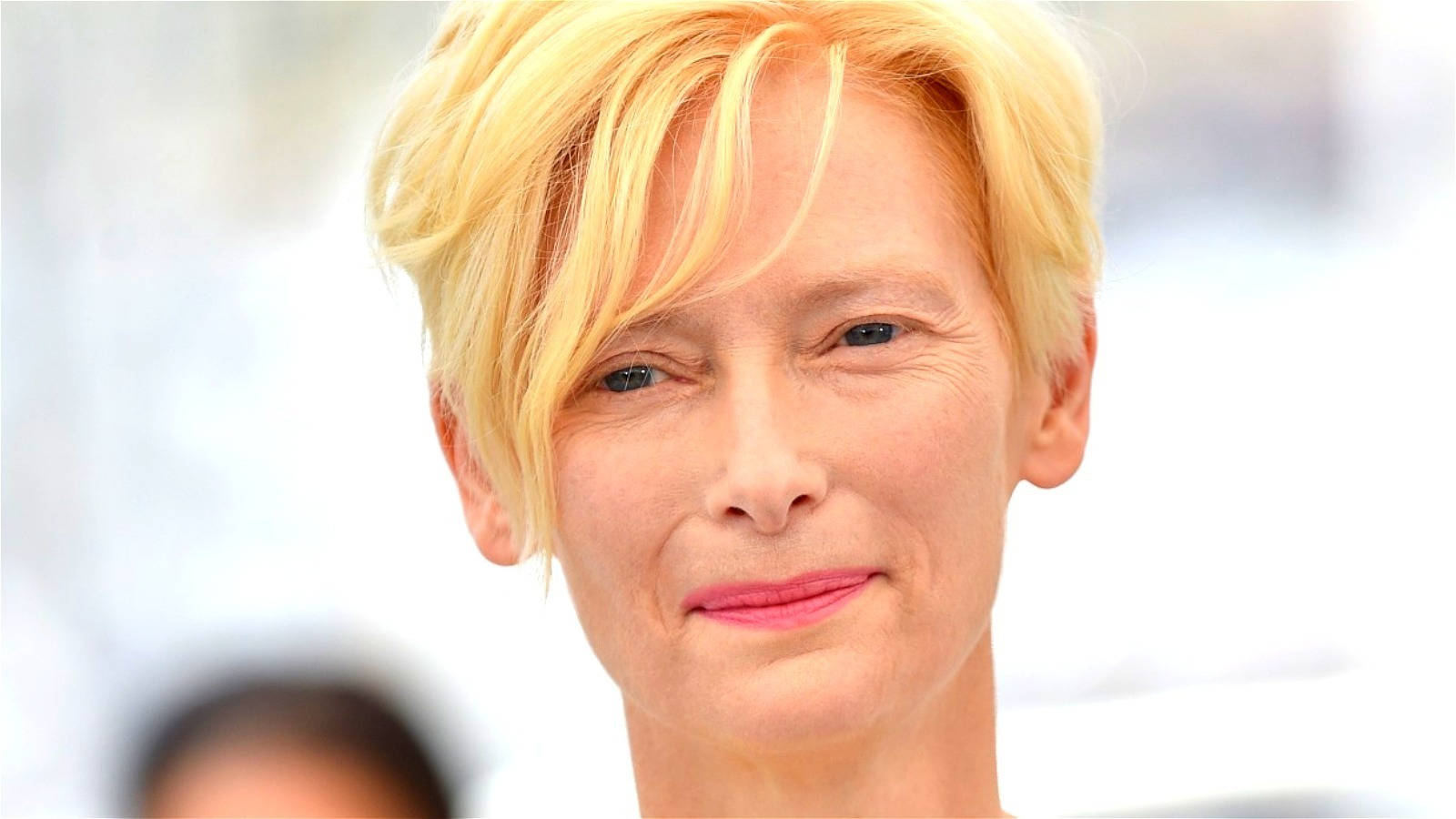 短金髮、塗粉紅色唇膏的女性溫柔微笑。