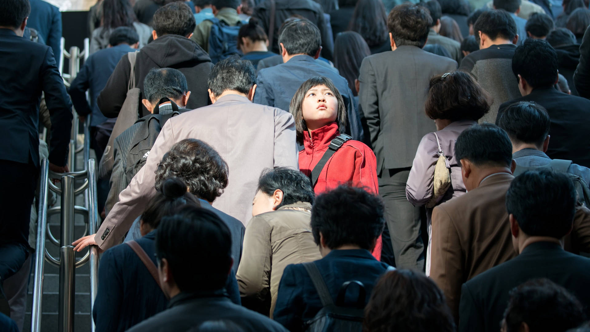 白天通勤時，年輕女子穿著紅色外套站在擁擠的自動扶梯上。