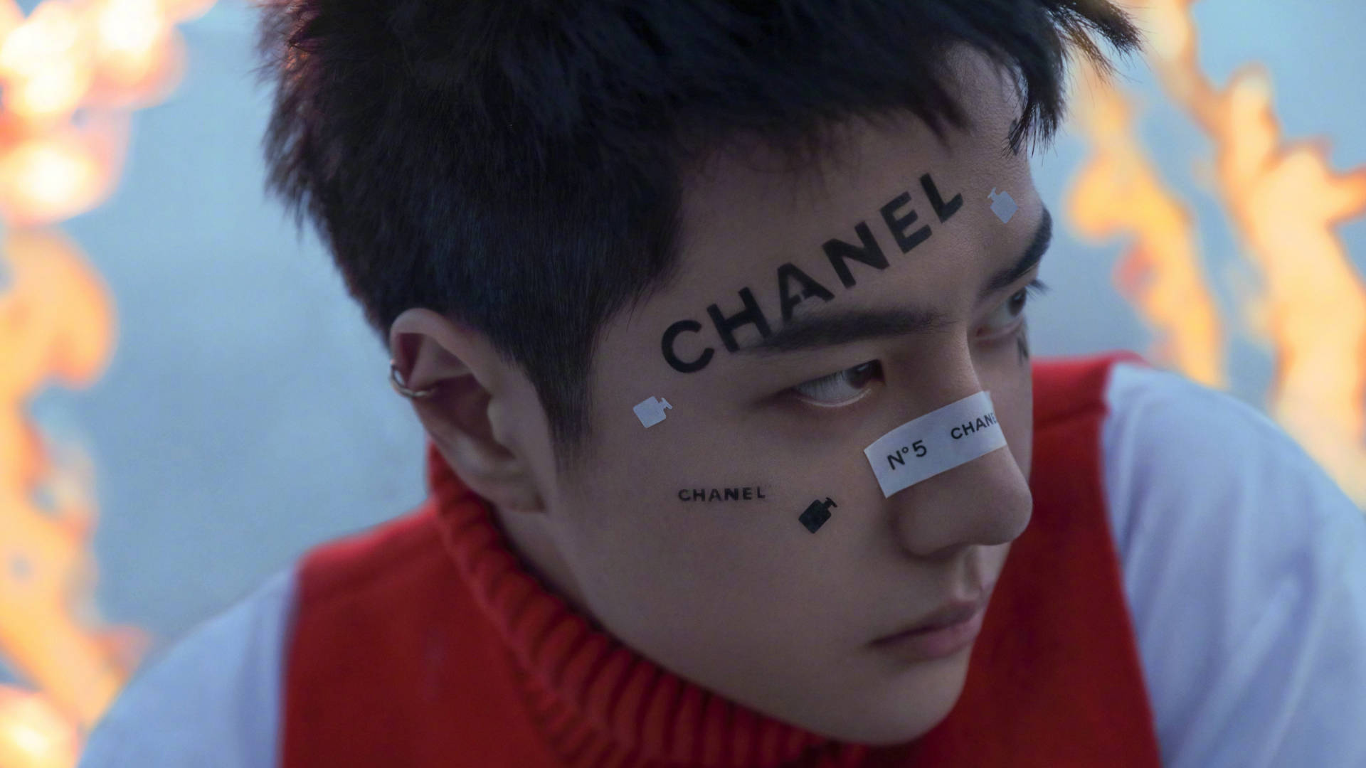 王一博香奈兒封面妝容 壁紙 — 一名年輕男子臉上寫著「CHANEL」和「N°5」，穿著紅色高領毛衣，背景是火熱的橙色和藍色。