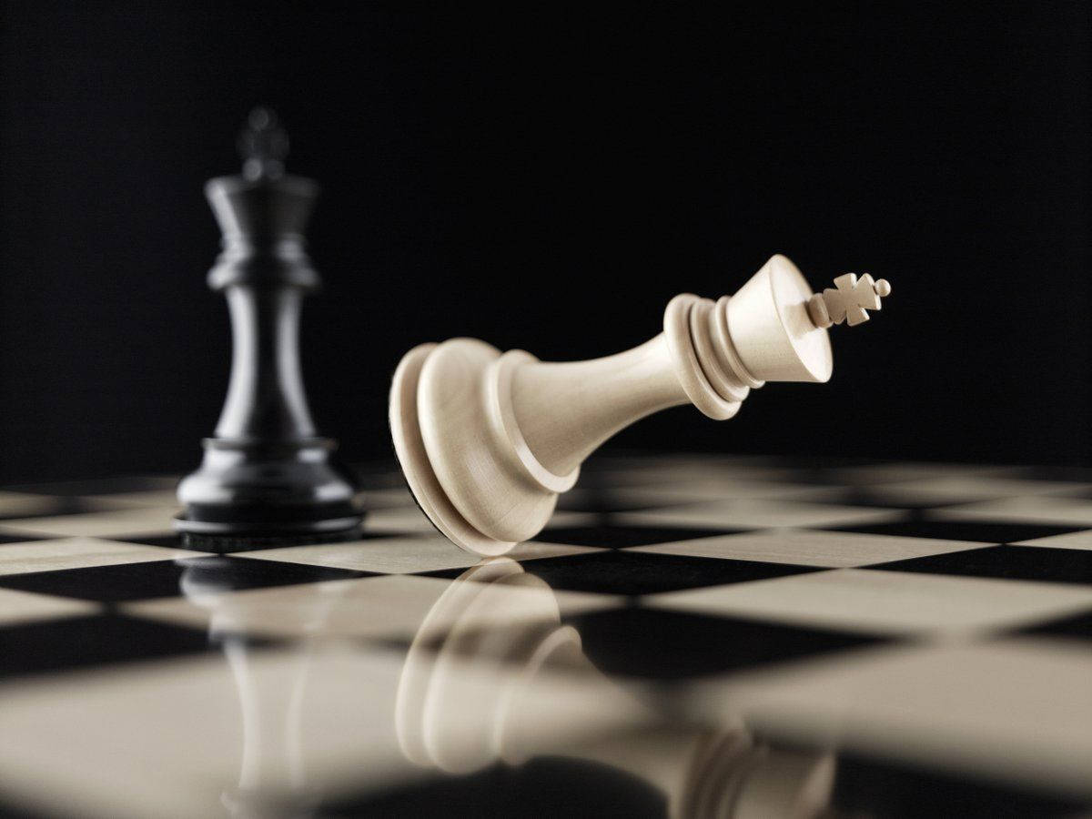 王權棋局 壁紙 — 一隻倒下的白色國王棋在光亮的棋盤上，旁邊站著一隻黑色國王棋，在戲劇性的燈光下敗陣。