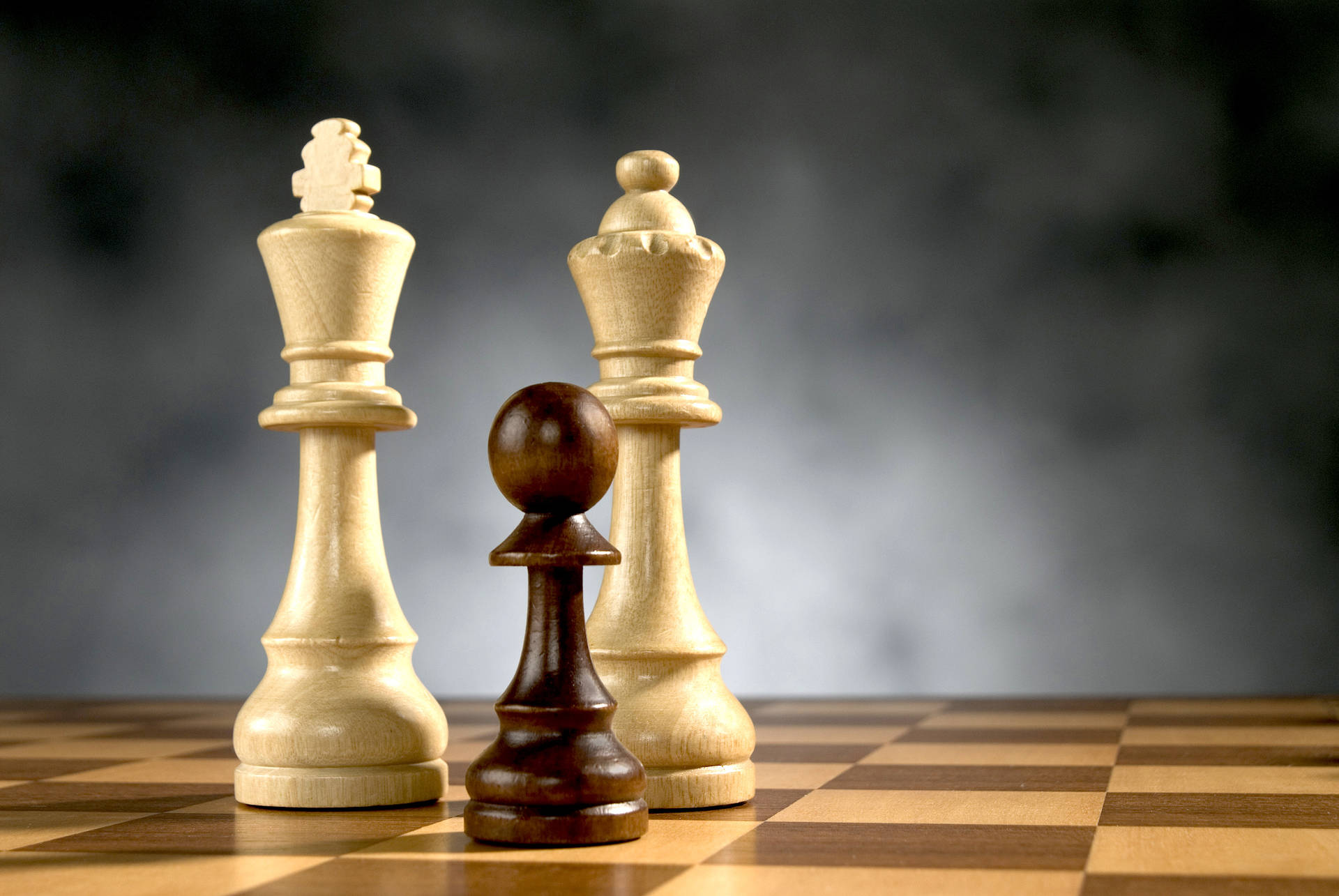 三個木製國際象棋棋子放在棋盤上，背景為煙灰色。