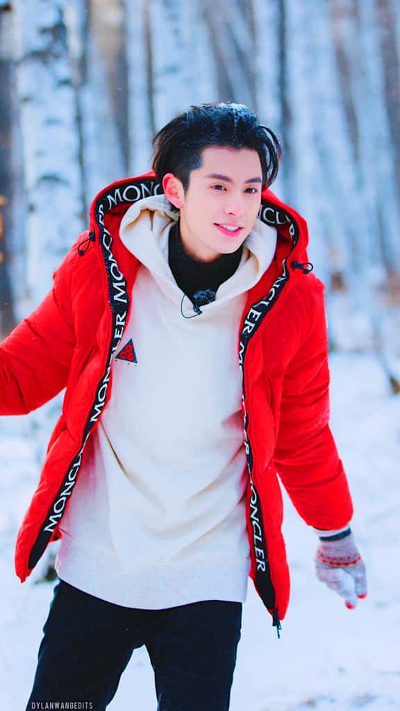 年輕男子身穿紅色冬季外套在雪地森林中微笑。