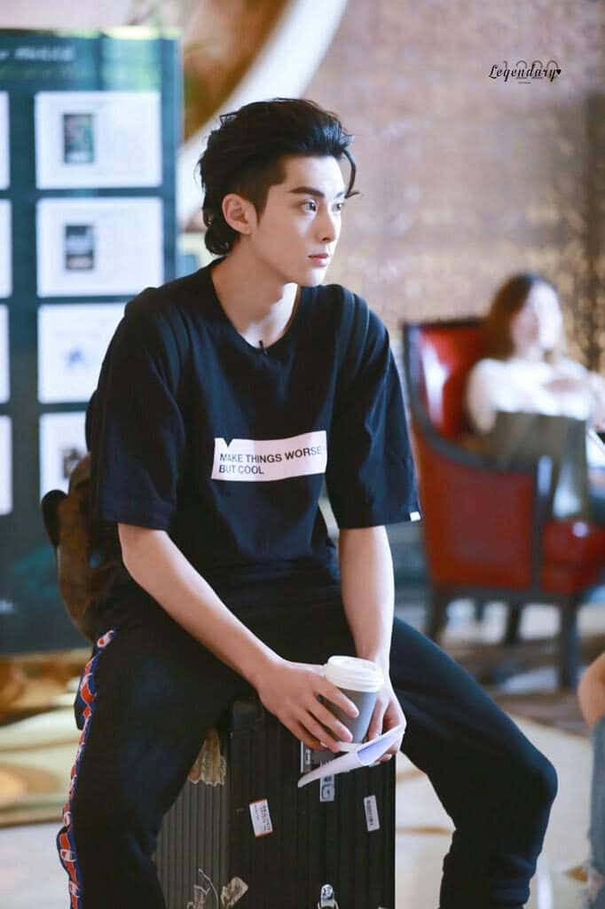 年輕男子坐在行李箱上手持咖啡杯