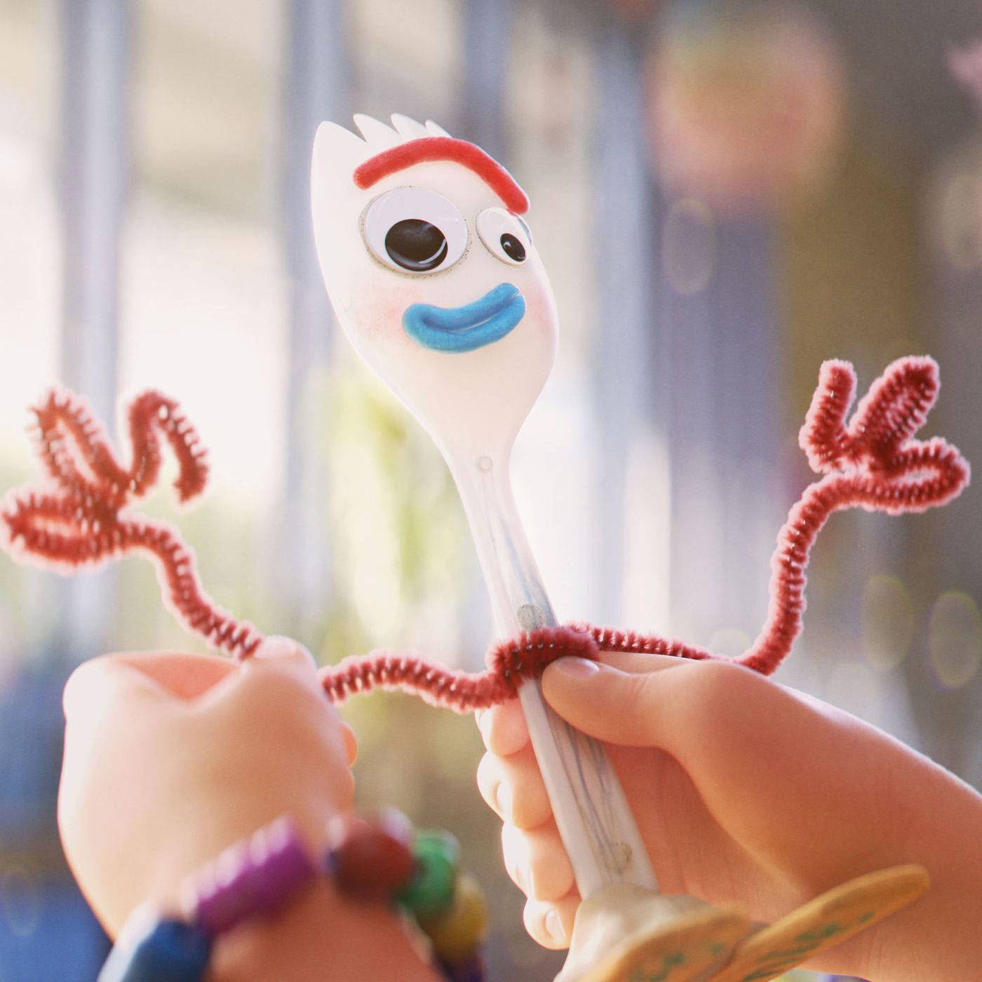 玩具總動員 Forky 筷子叉 壁紙 — 一個快樂的動畫叉子，帶有管道清潔器手臂和藍色微笑，被孩子的手在柔和日光中握住。
