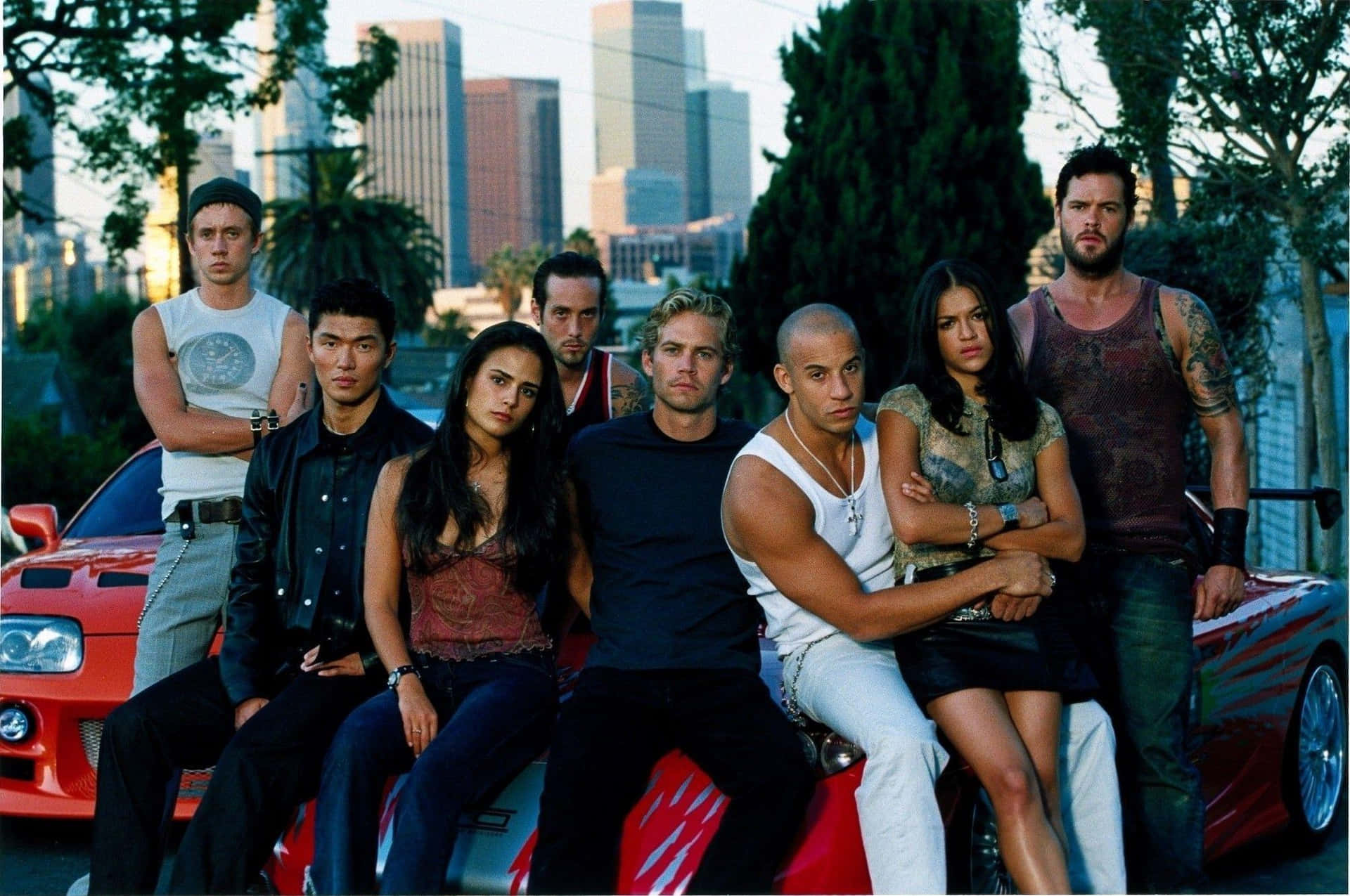 Fast and Furious 演員在日落時分的城市中，在一輛紅色汽車上擺姿勢。