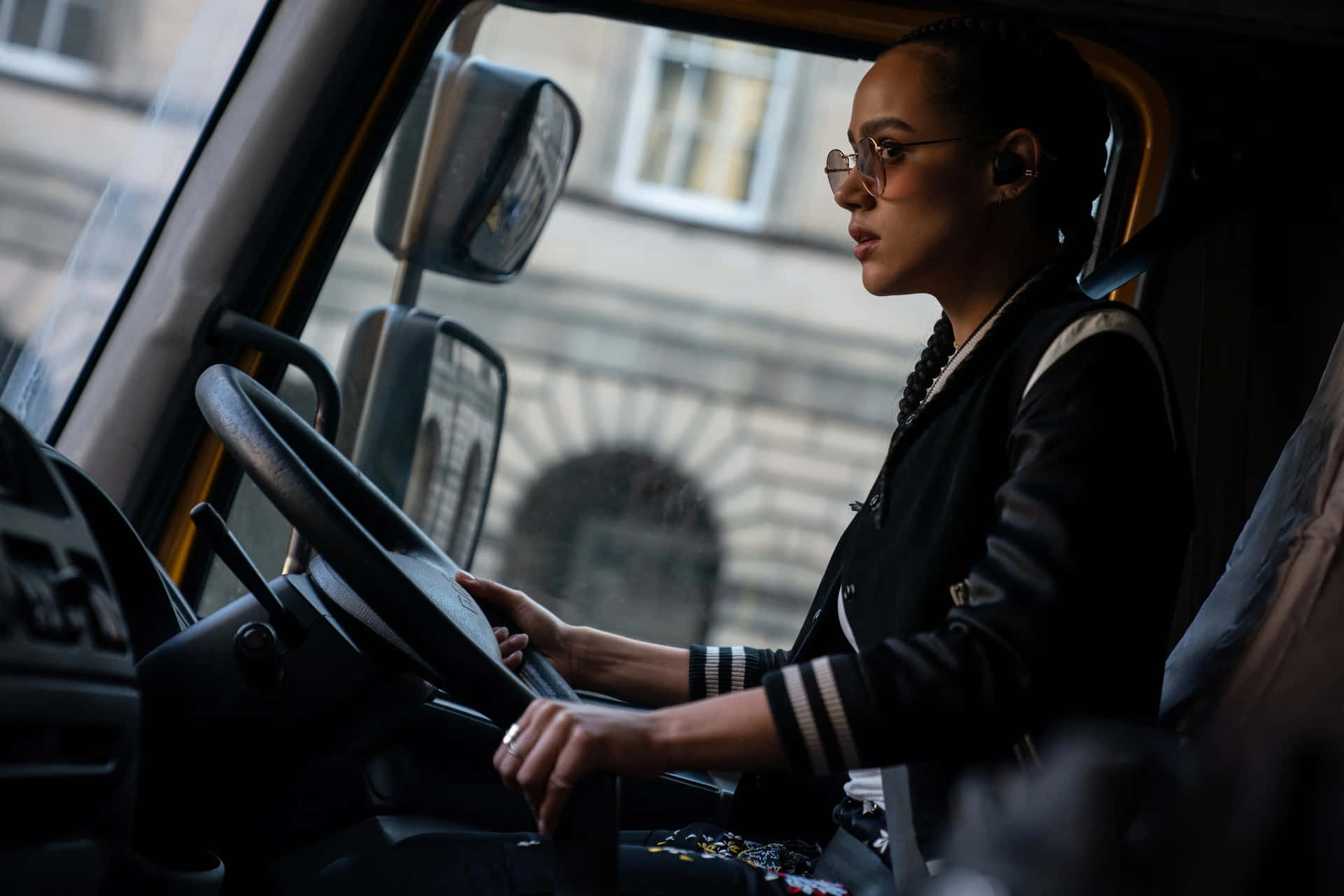 一位戴眼鏡的女性駕駛貨車行駛在城市街道上。