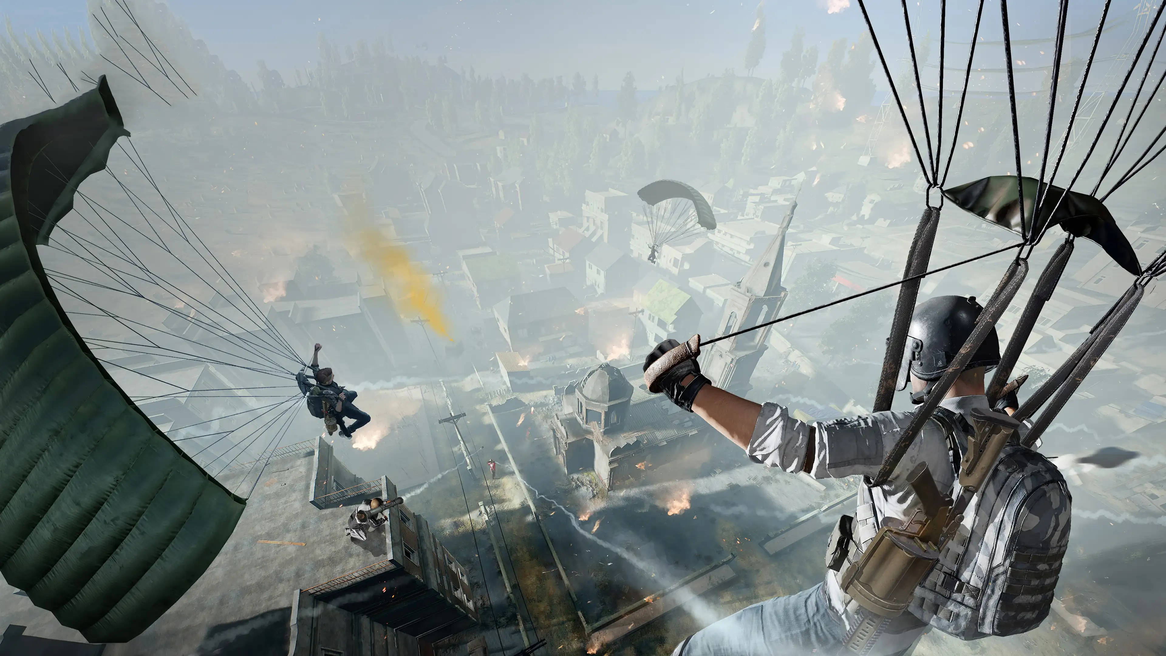 Pc Gaming 桌布 壁紙 — 玩家跳傘進入一個被戰爭摧毀的城市景觀，下方有爆炸和煙霧。
