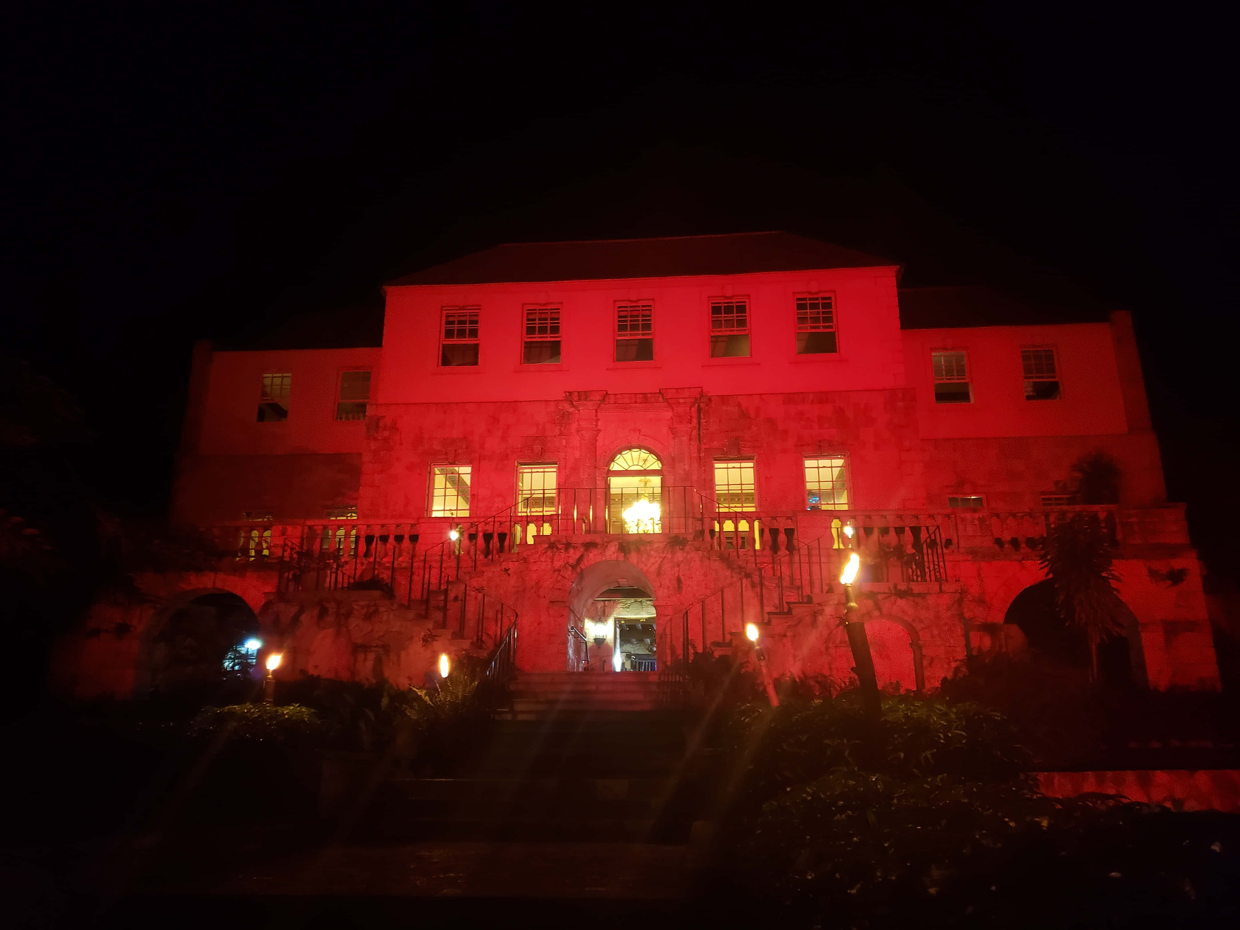 玫瑰廳大宅夜間紅燈照明 壁紙 — 一座宏偉的石建築在夜晚沐浴在詭異的紅光中，發光的窗戶和火炬照亮了樓梯。