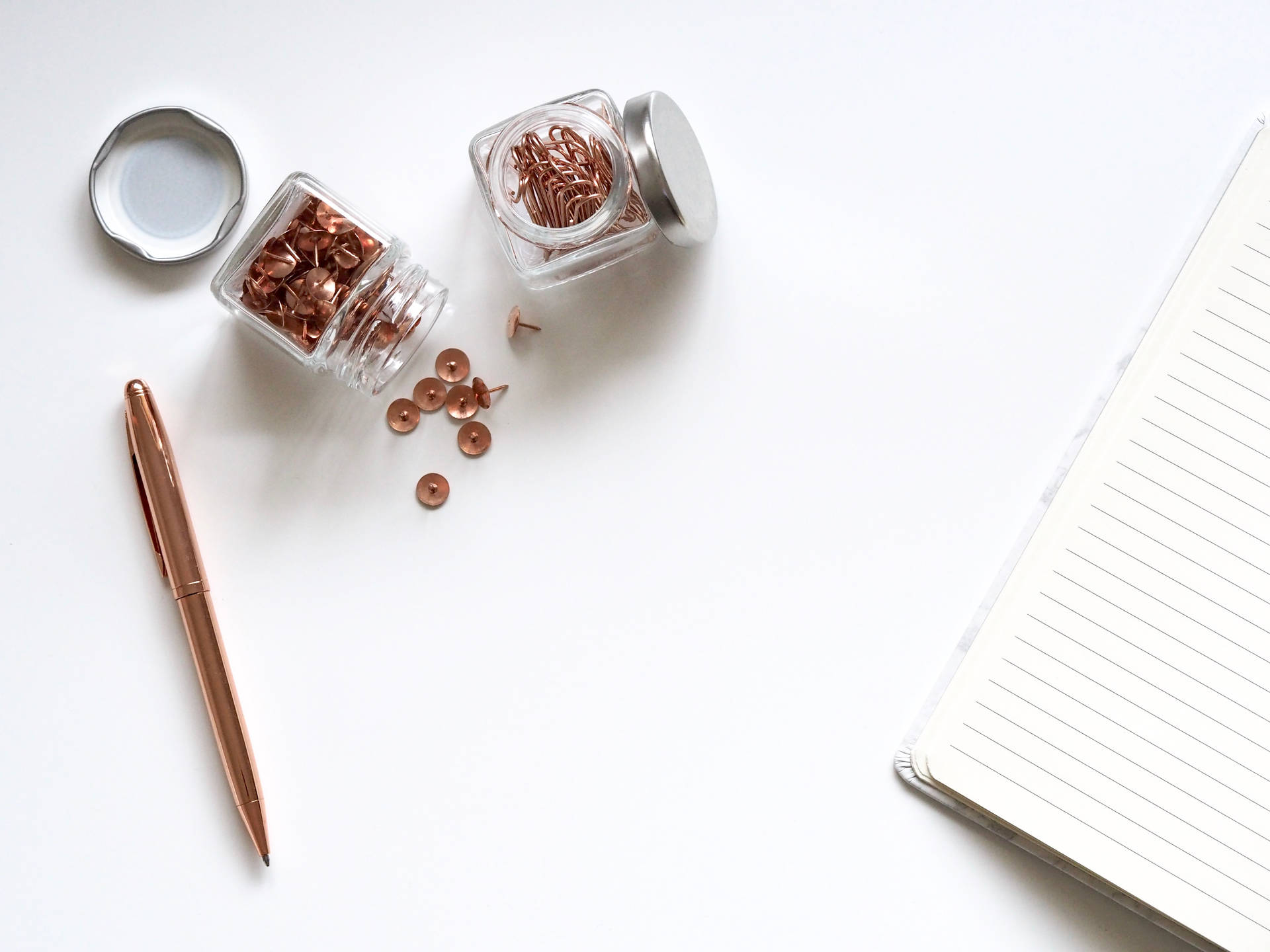 Rose gold stationery items on a white desk surface including push pins and pen.