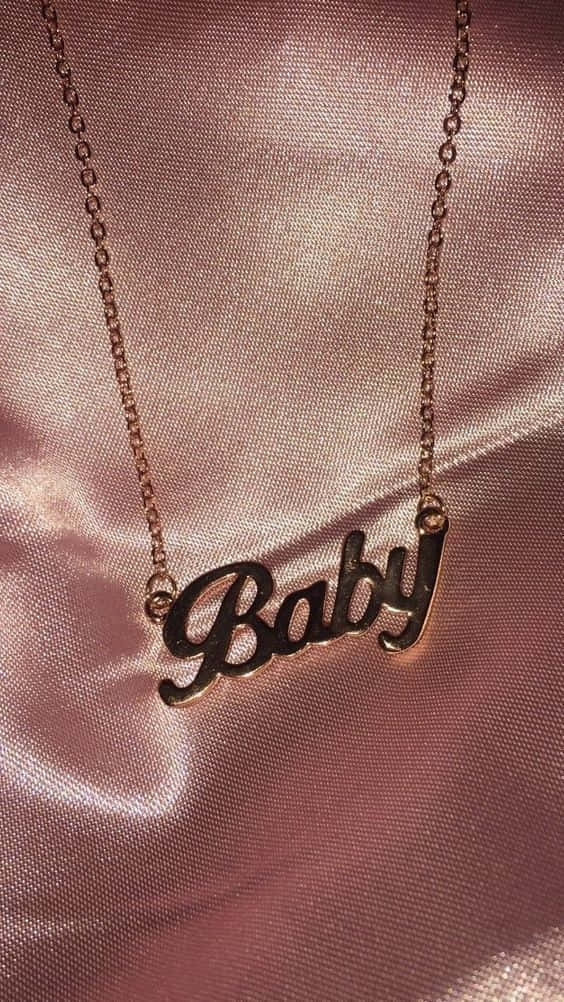 玫瑰金「Baby」吊墜項鍊放在粉紅色緞面布料上。