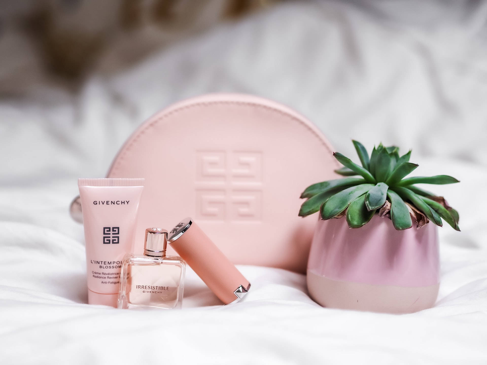 粉紅色 Givenchy 化妝品和多肉植物在白色床上。