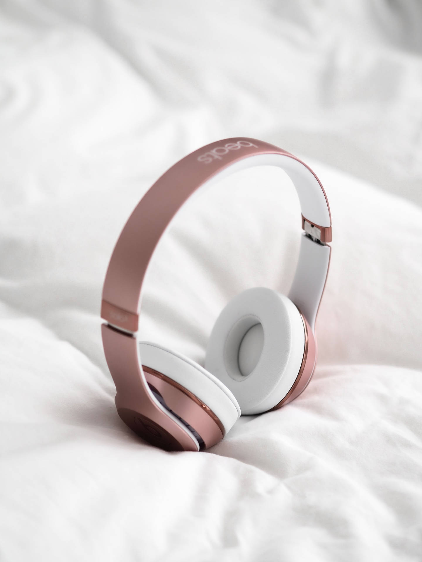 白色床單上的玫瑰金色 Beats 耳機