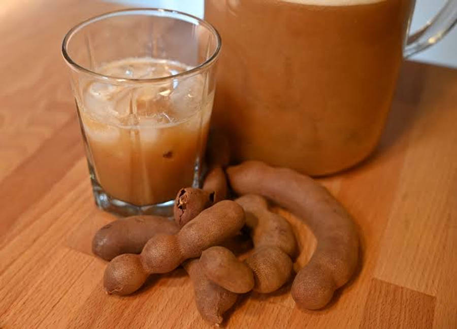 玻璃杯盛裝清爽酸角茶 壁紙 — 一杯冰凍羅望子飲品，連同整條羅望子莢，放在溫暖的木桌上。