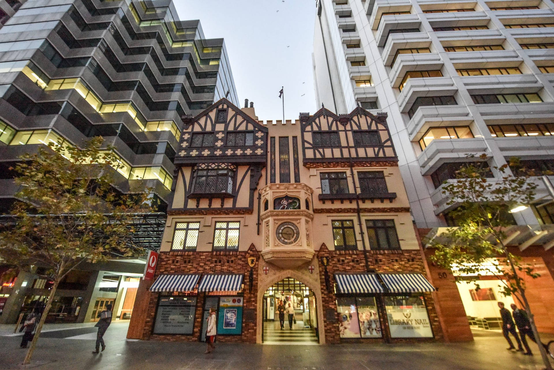 都鐸風格建築被現代摩天大樓環繞，夜晚有人行走。