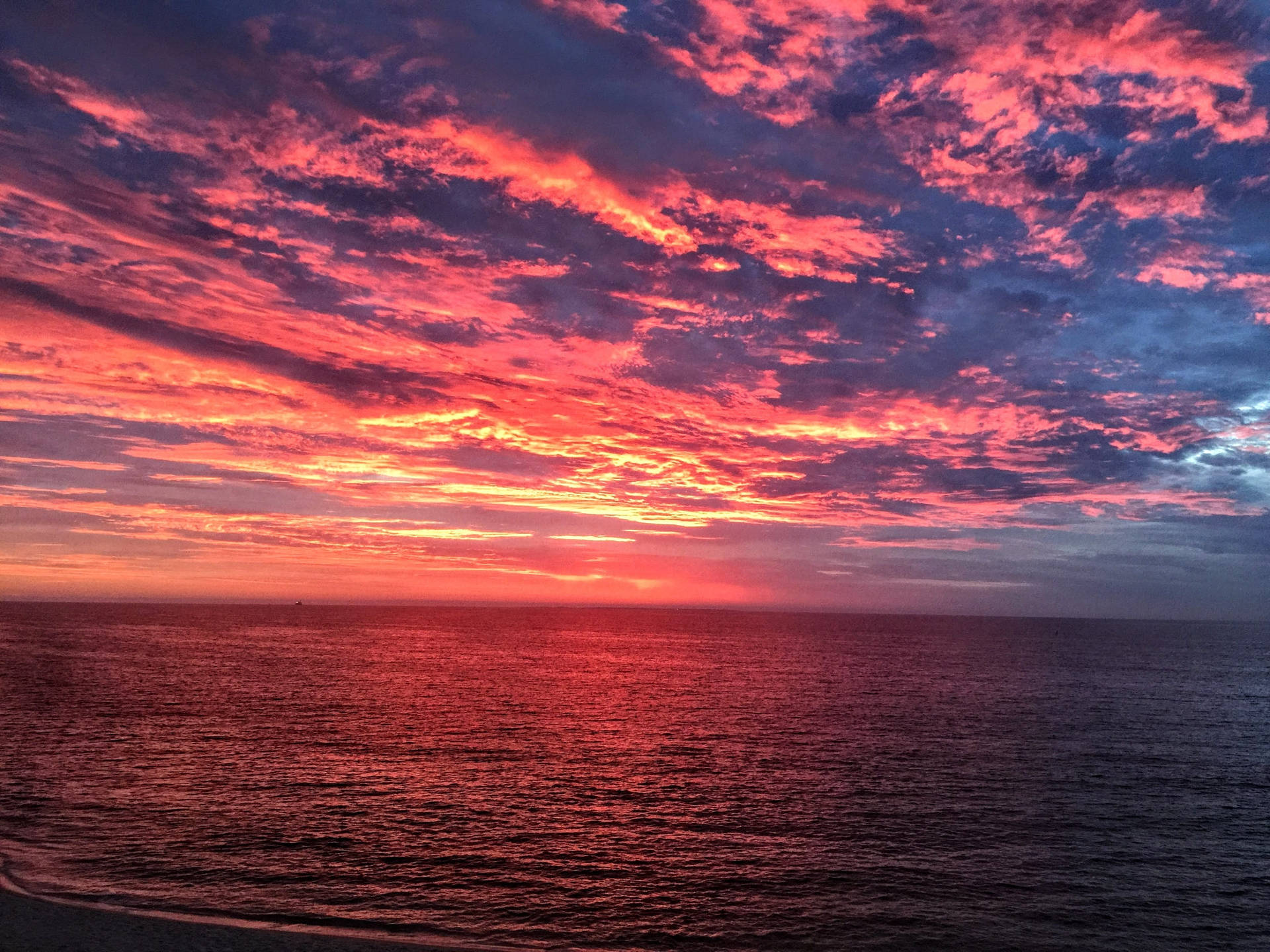 黃昏時分，平靜的海面上空呈現鮮豔的紅色和橙色日落雲彩。